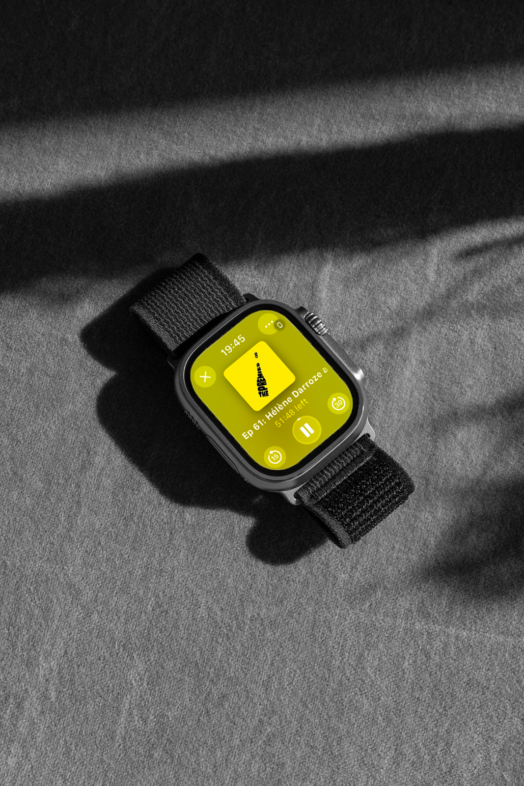 A smartwatch with a black band displaying a podcast app on a dark gray surface.