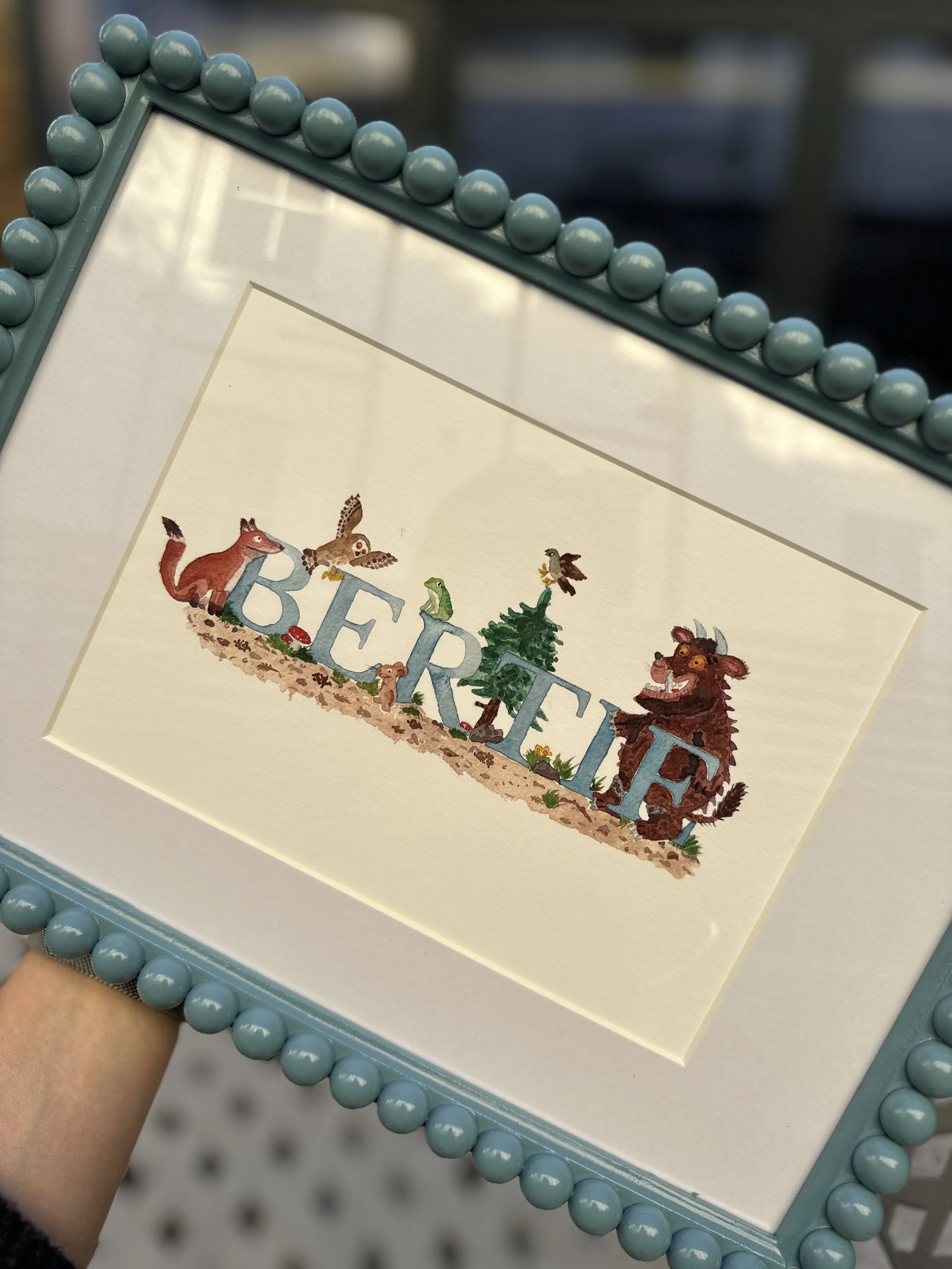 Decorative picture frame with the word "BERTIE" spelled out in colorful letters, surrounded by woodland animals and trees.