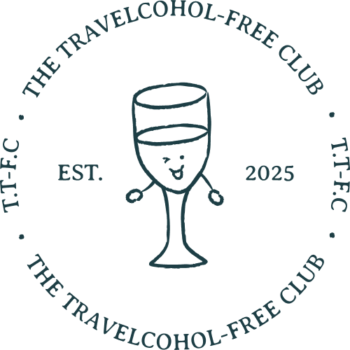 A circular logo for 'The Travelcohol-Free Club' featuring a glass of wine with a happy face, and the text 'EST. 2025' around it.