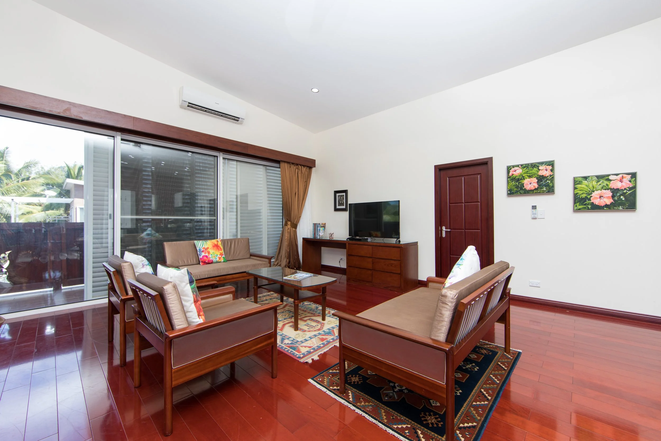 2 Bedroom Premium Villa living room with hardwood floors, wooden furniture, a flat-screen TV, a sliding glass door with a balcony, and original paintings