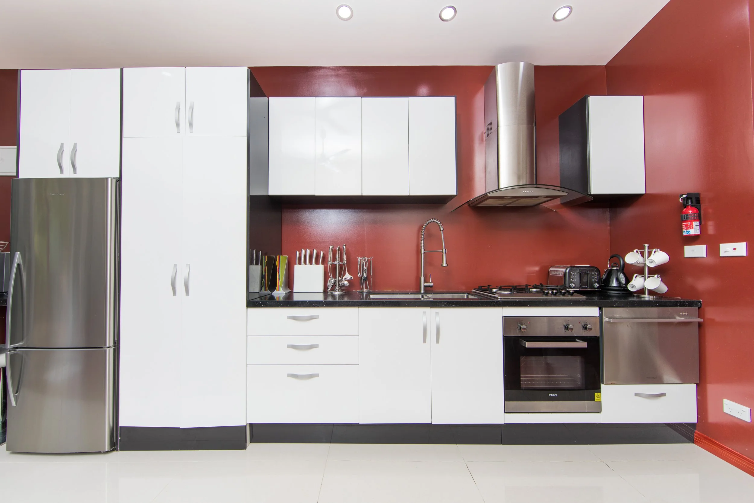 Honeymoon Villa modern kitchen with white cabinets, black countertops, stainless steel appliances, red wall, and various small appliances.