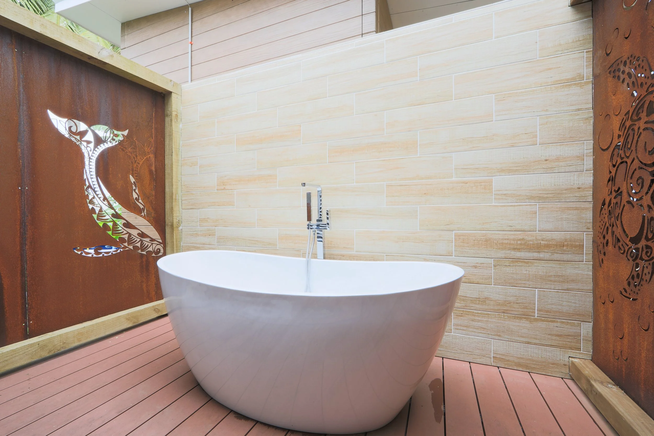 Honeymoon Villa outdoor bathtub on wooden deck with beige tiled wall and decorative metal panels featuring whale and turtle motifs.