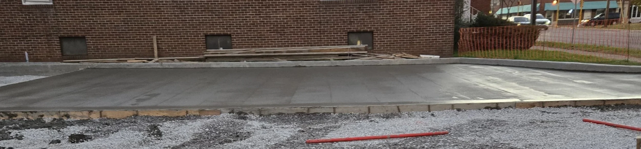 Construction site with freshly poured concrete sidewalk and brick building in background.