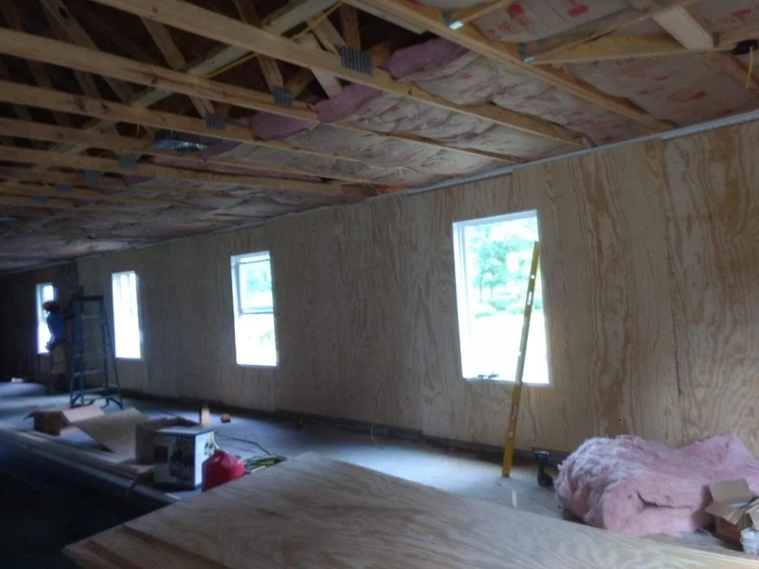 Interior of a building under construction with unfinished walls and ceiling, pink insulation, and construction tools.