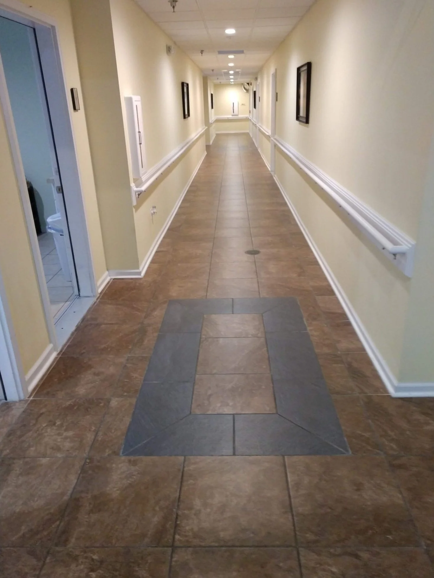 Empty hallway in a building with beige walls and brown tile flooring, featuring a raised platform near the foreground.