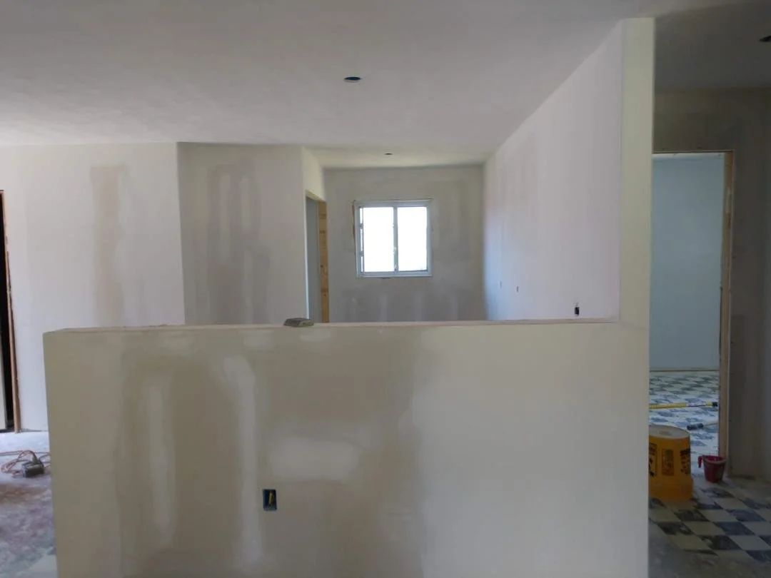 Interior of a house under construction with drywall partly installed, unfinished walls, and construction materials on the floor.