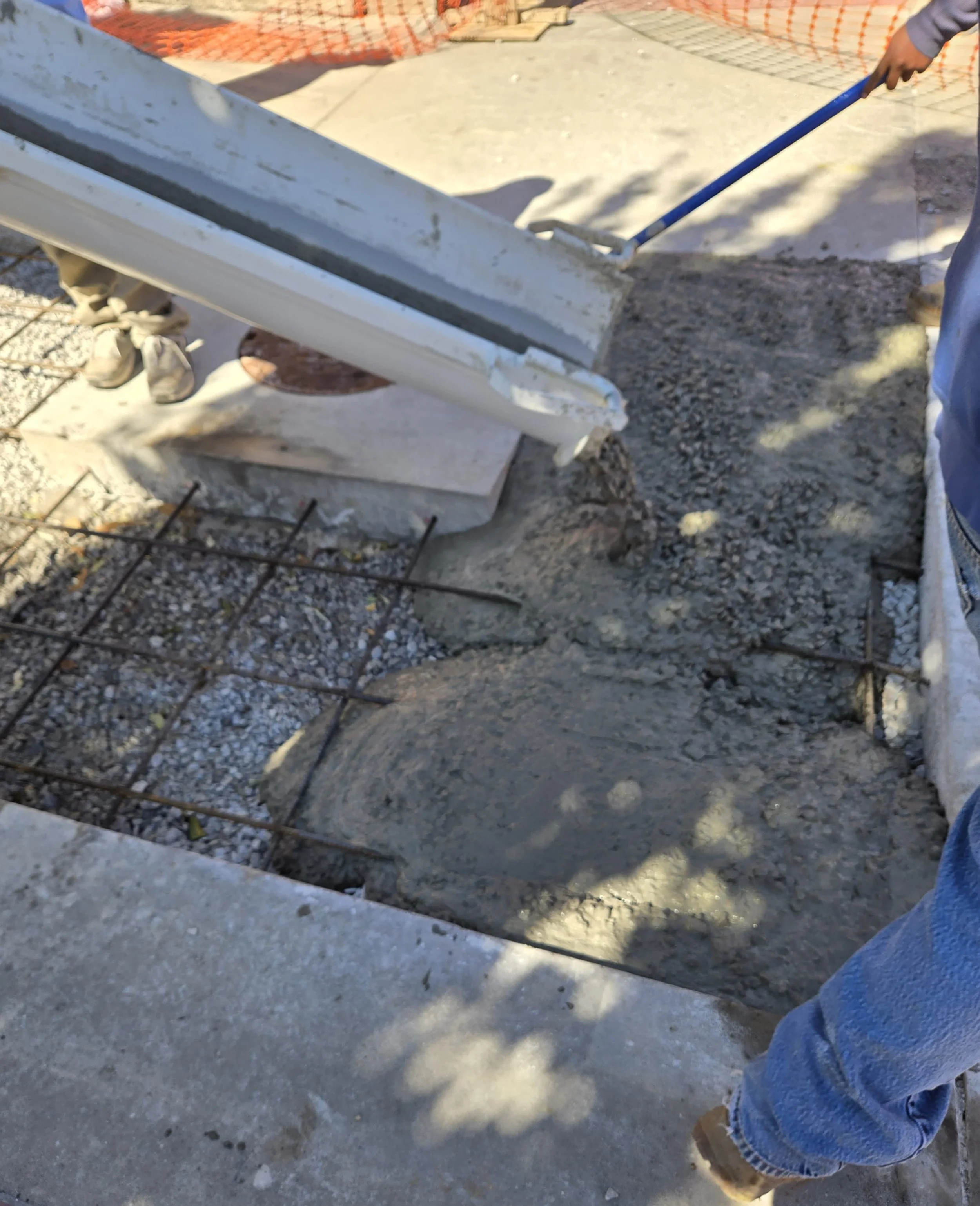 Construction worker pouring wet concrete over rebar for a sidewalk or foundation at a construction site.