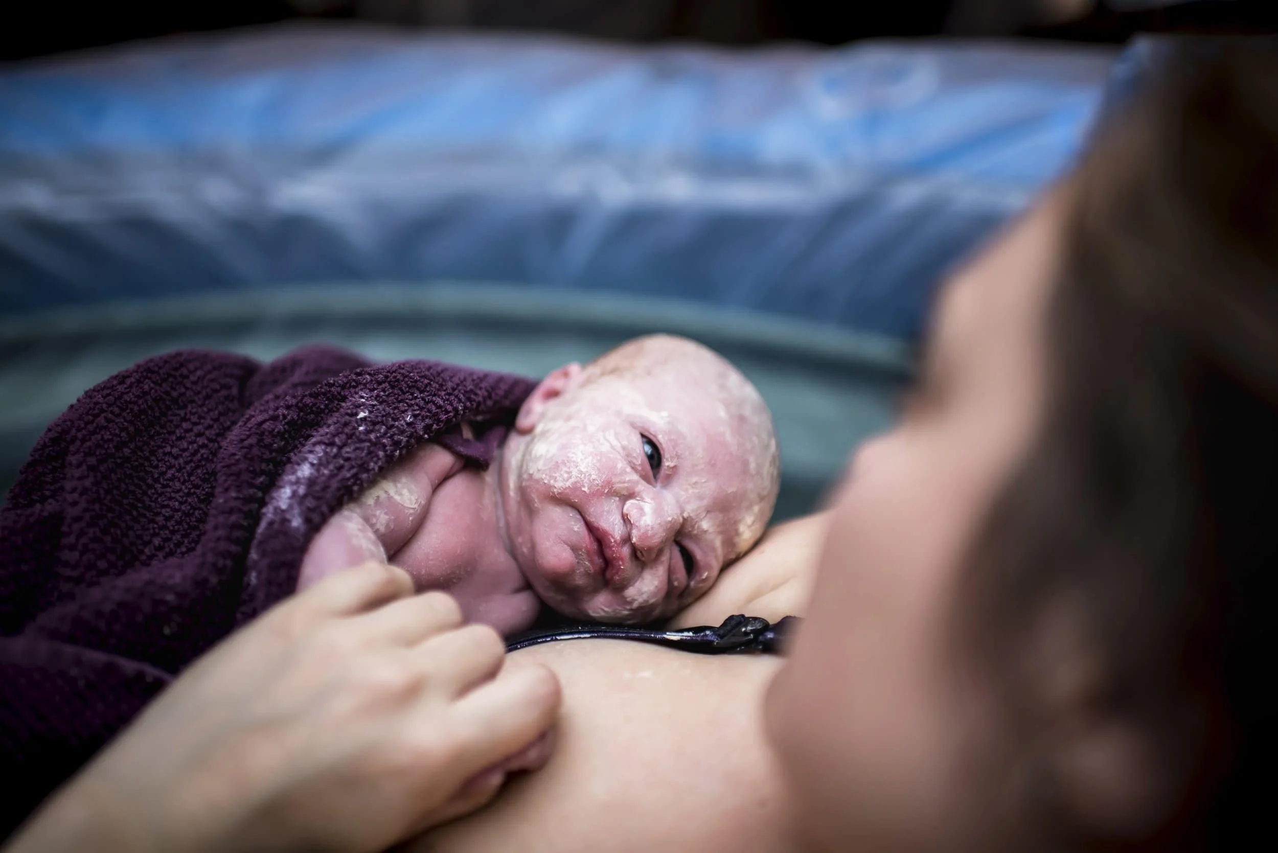 Brand new baby born at home in the water looking up at mom in birth tub in Ottawa.