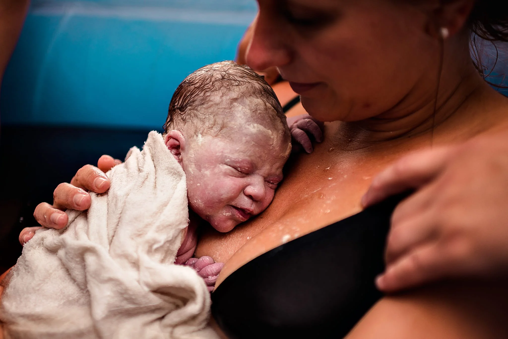 A woman holding her newborn baby close to her chest during childbirth, with both covered in amniotic fluid.