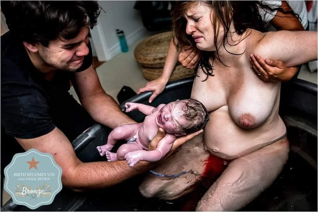 Newborn baby being born into a birthing tub, with a woman, likely the mother, in the water and several hands supporting her during labor.