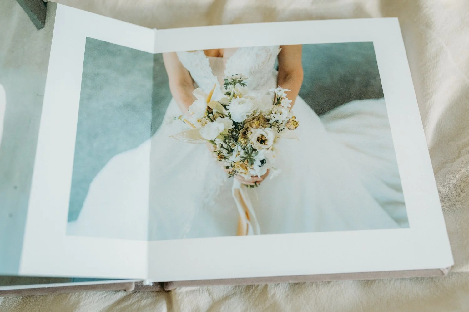 Hochzeitsfotobuch mit Bild einer Braut in weissem Kleid, die einen Blumenstrauss hält, aufgenommen von oben.
