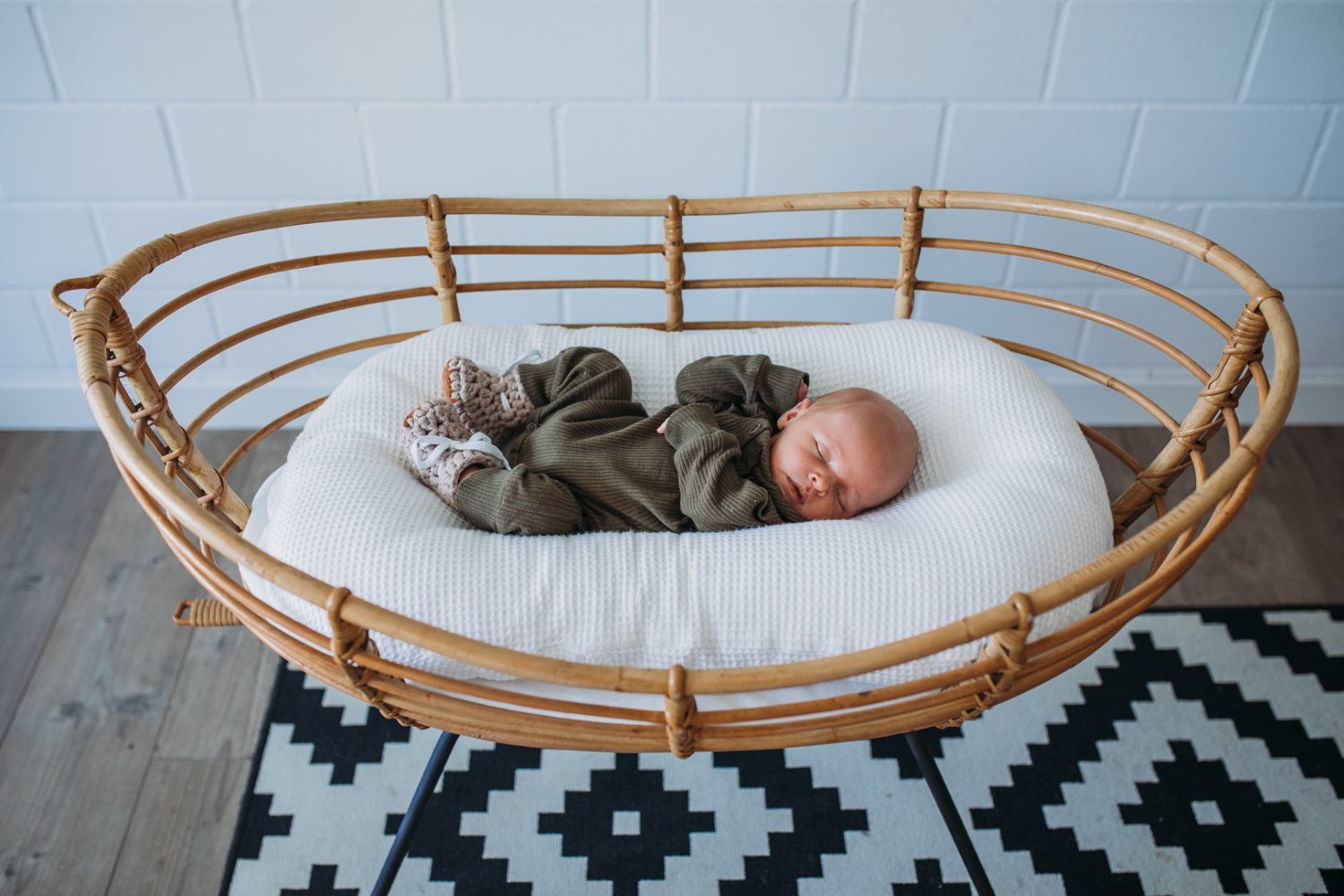 Ein schlafender Säugling liegt in einem Korbbettchen auf einer weissen Matratze.