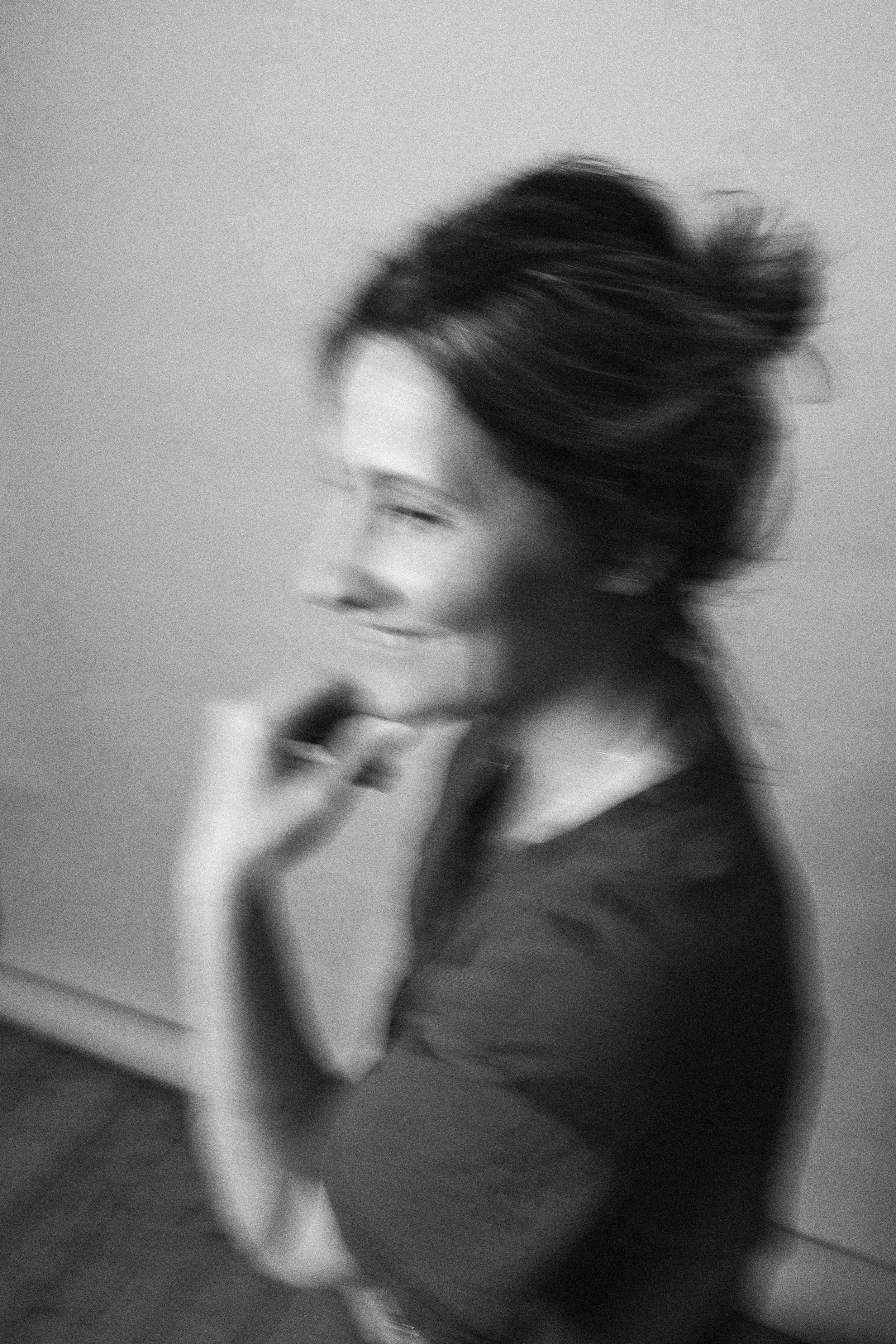 Schwarz-weiß-Foto einer lachenden Frau mit unordentlichem Haar, die neben einer weißen Wand steht.