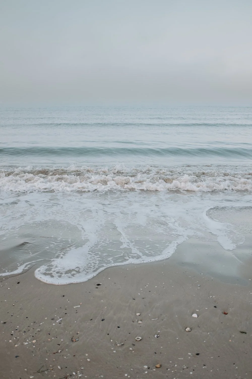 Ein ruhiger Strand mit sanften Wellen und sandigem Ufer, im Hintergrund der Himmel.