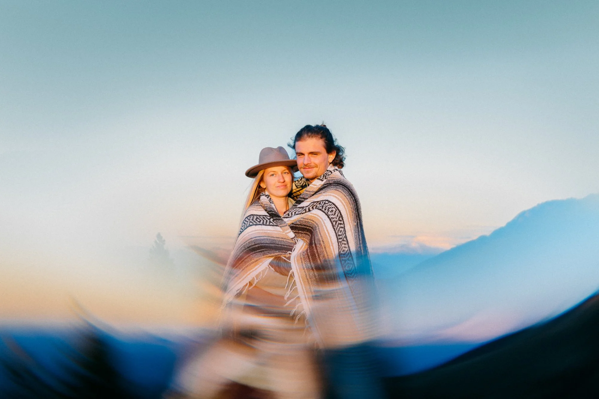 Ein Paar umarmt sich  bei Sonnenuntergang, umwickelt mit einem mehrfarbigen Decke in braunen Tönen im mexikanischen Stil.