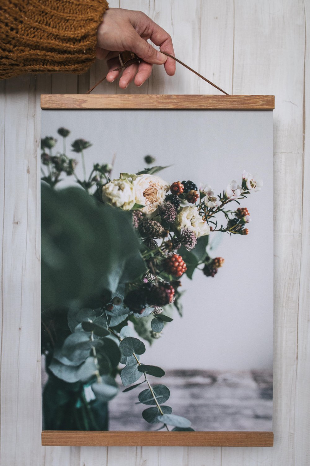 Eine Hand, die eine Kordel an einem Holzrahmen eines Wandbildes mit Blumen hält.