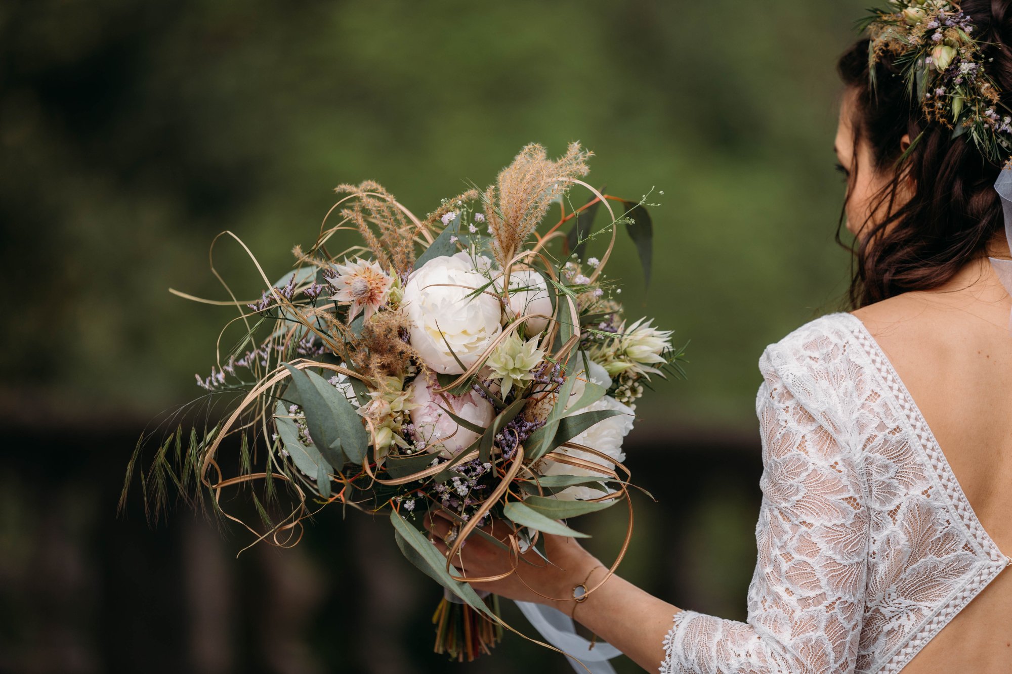 Frau in weissen Spitzenkleid hält einen Strauss aus weissen und pastellfarbenen Blumen, Nahaufnahme.