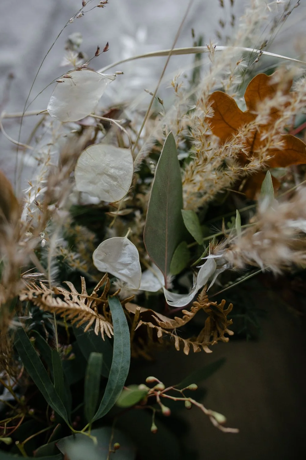 Nahaufnahme eines Blumenstrausses mit grünen Blättern, braunen Blättern und trockenen, hellen Gräsern.