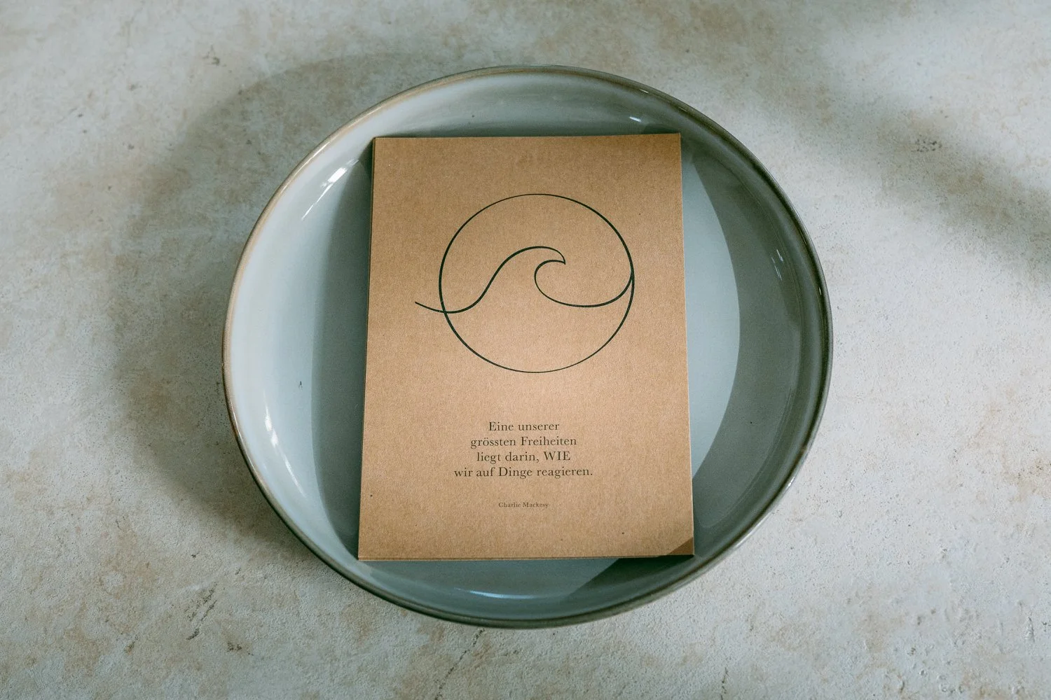 Karte mit einer Welle und einem Kreis, auf einem grauen Teller liegt.