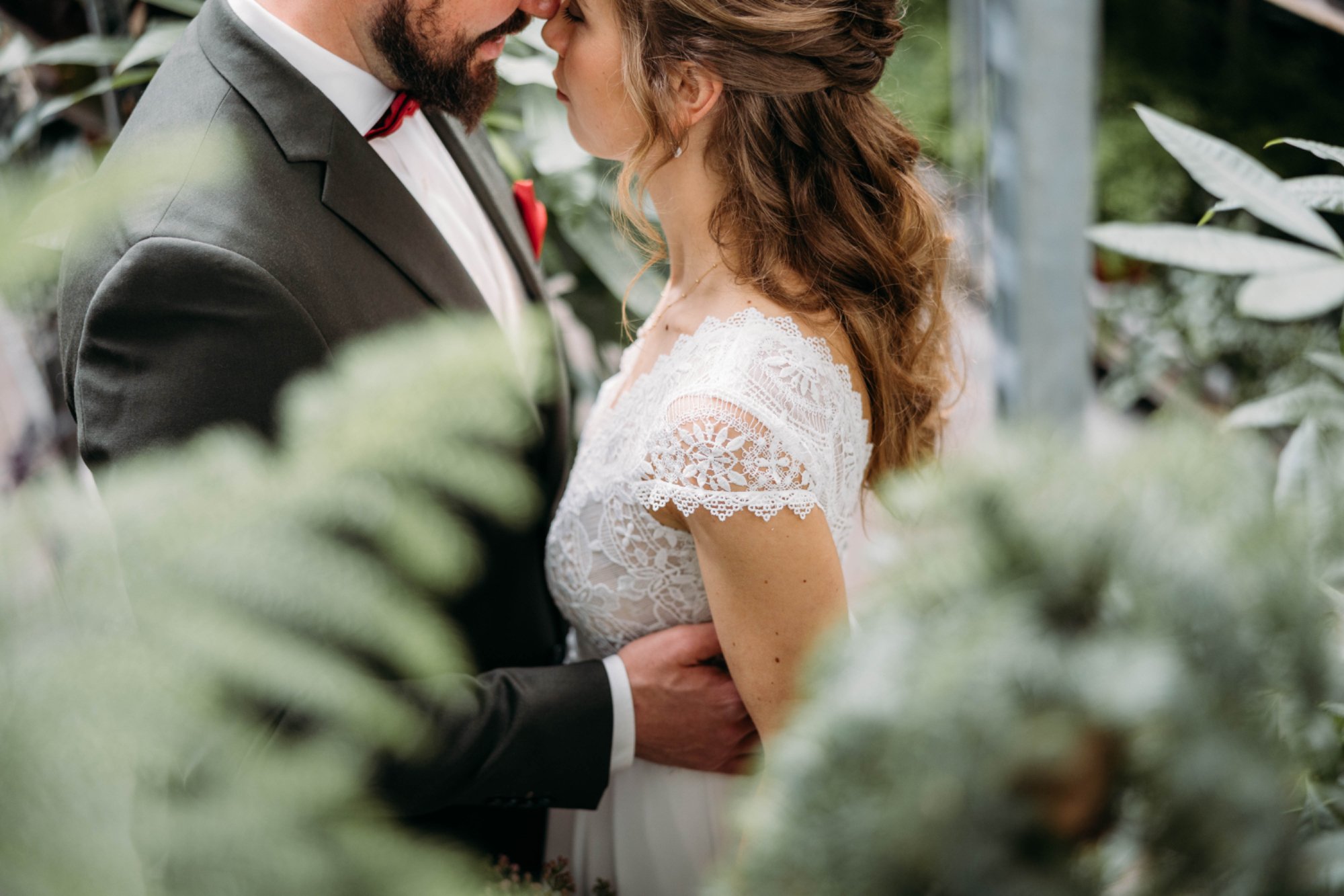 Ein verliebtes Brautpaar, das sich anschaut, umgeben von grünen Pflanzen, im romantischen Moment mit gesenkten Köpfen.