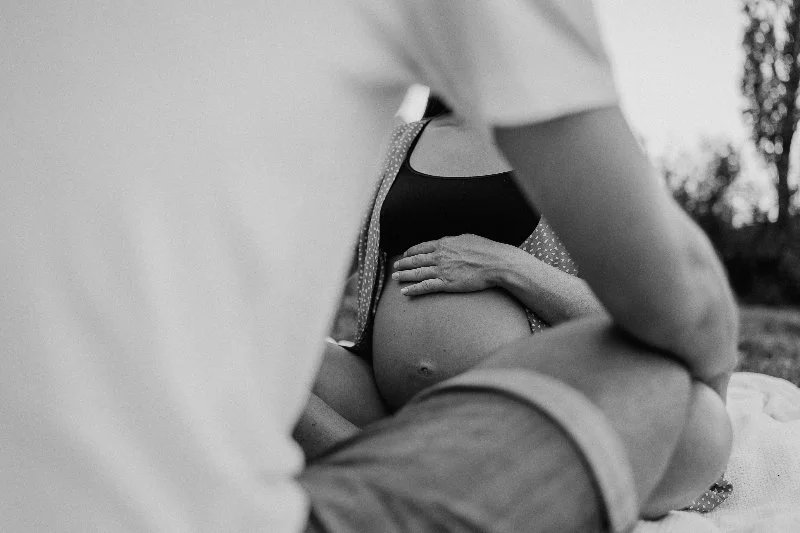 Schwangere Frau, die ihren Babybauch hält, draussen im Freien, schwarz-weisses Foto.