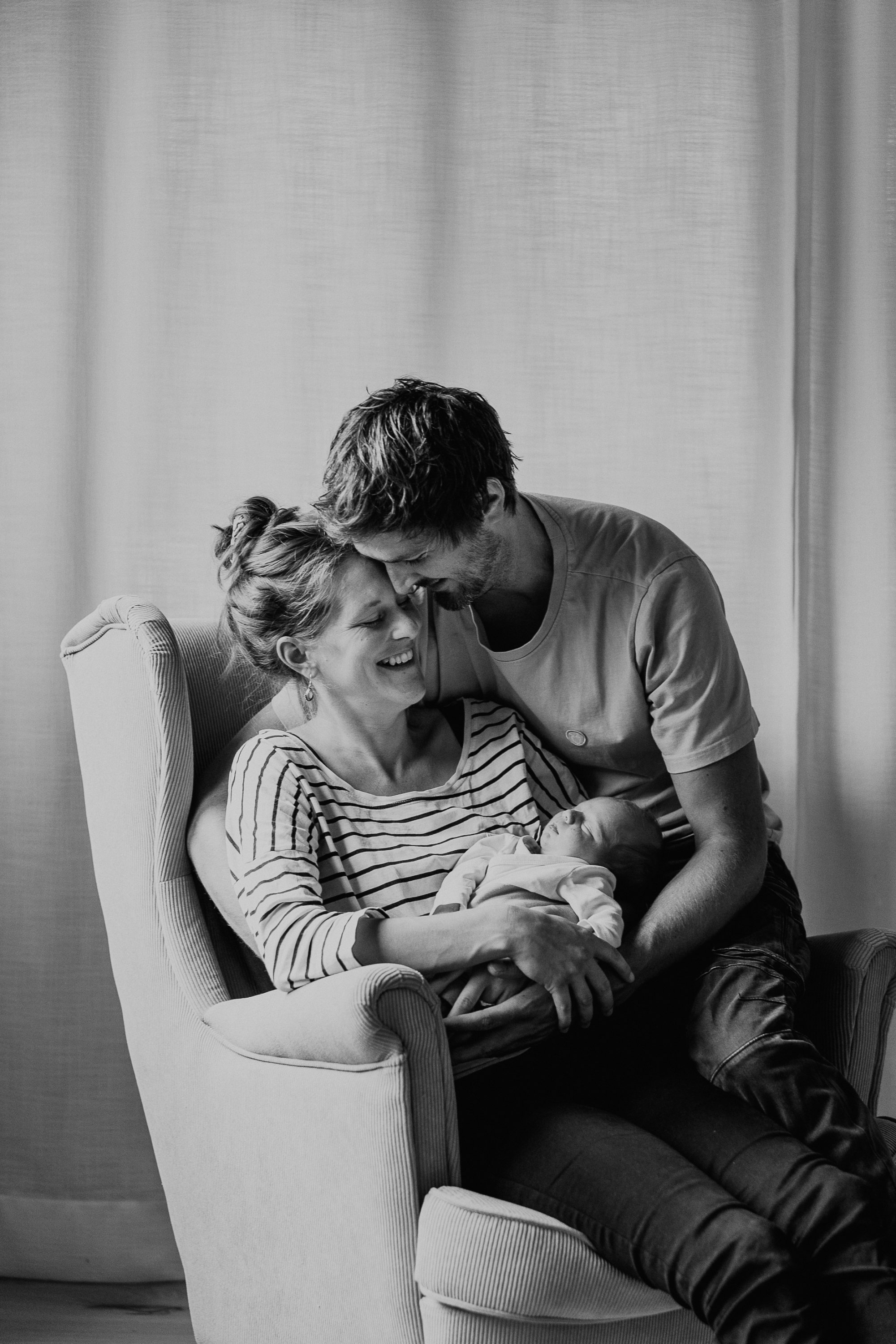 Ein glückliches Familienfoto mit einer Mutter, einem Vater und einem neugeborenen Baby, schwarz-weiß aufgenommen.