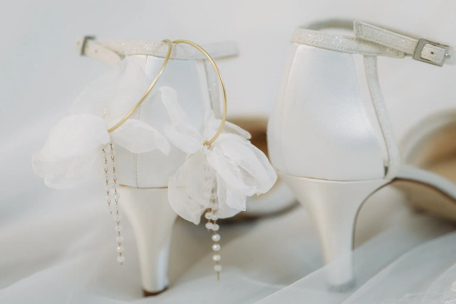 Weisse Hochzeitsschuhe mit hoher Absätze, verziert mit Schleifen und Perlen, auf einer weissen Oberfläche