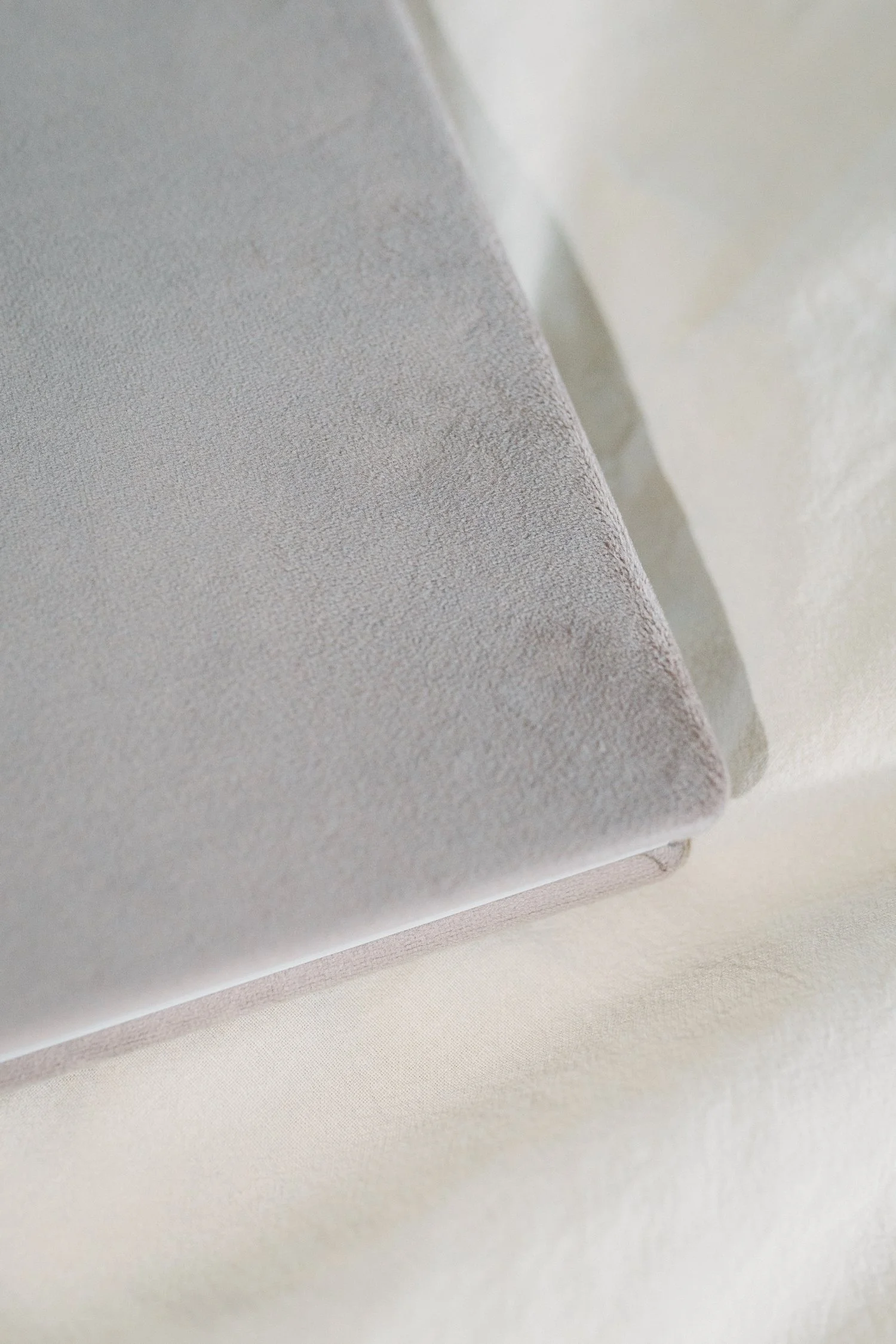 Nahaufnahme eines hellgrauen, samtartigen Stoffes auf einer weissen Oberfläche.