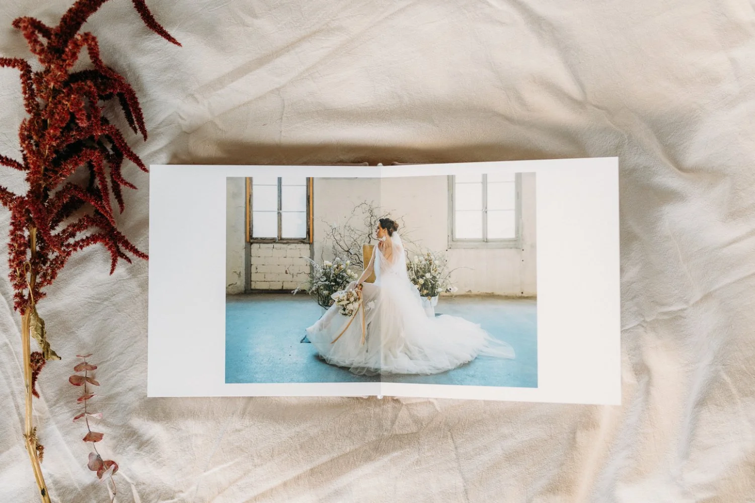 Aufnahme Hochzeitsalbum von oben: aufgeklappt sieht man eine Braut in einem weissen Kleid auf einem braunen Stuhl in einem Raum mit grossen Fenstern, Pflanzen im Hintergrund.