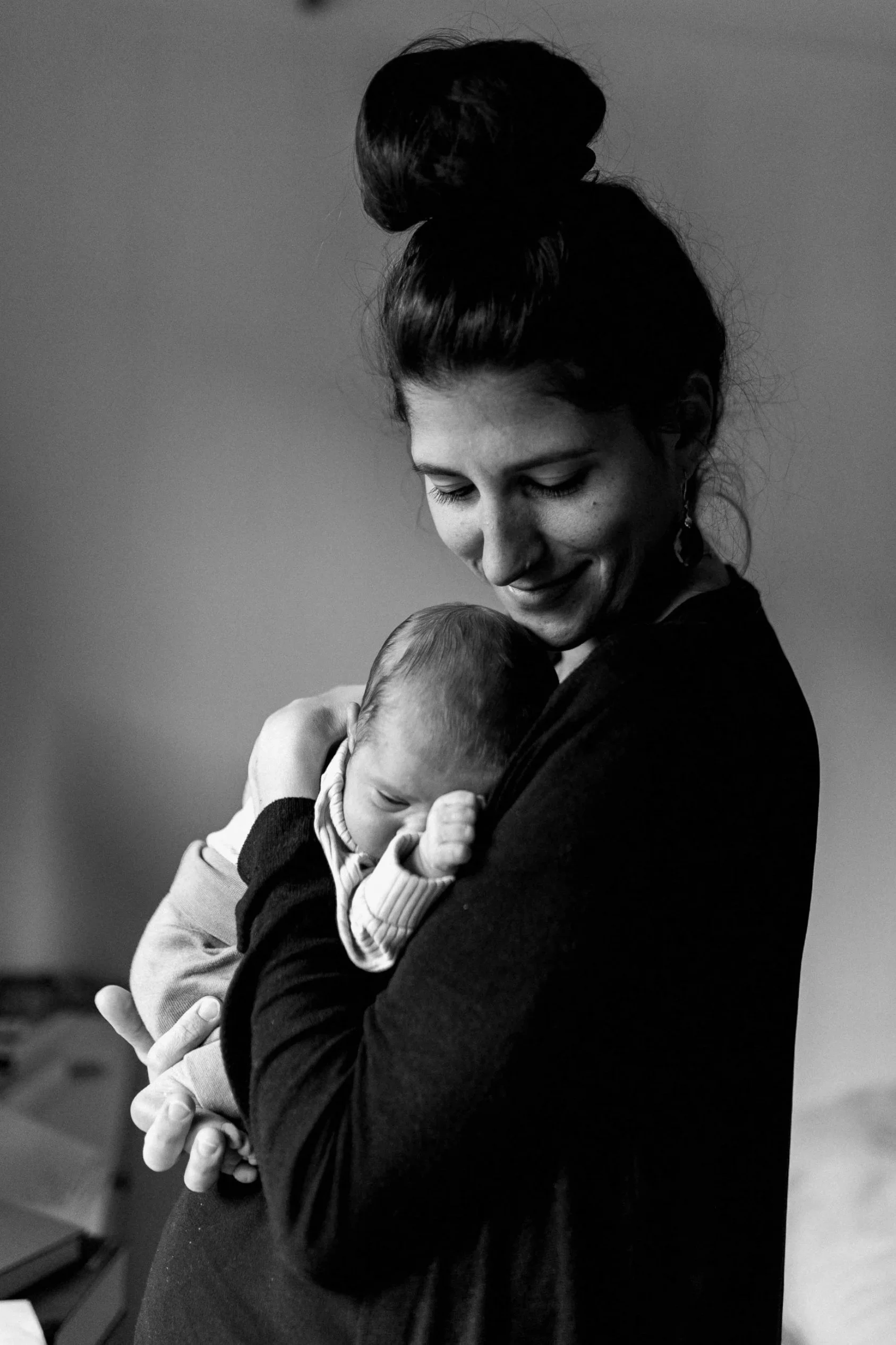 Frau hält ein schlafendes Baby in den Armen, das sich liebevoll an sie kuschelt.