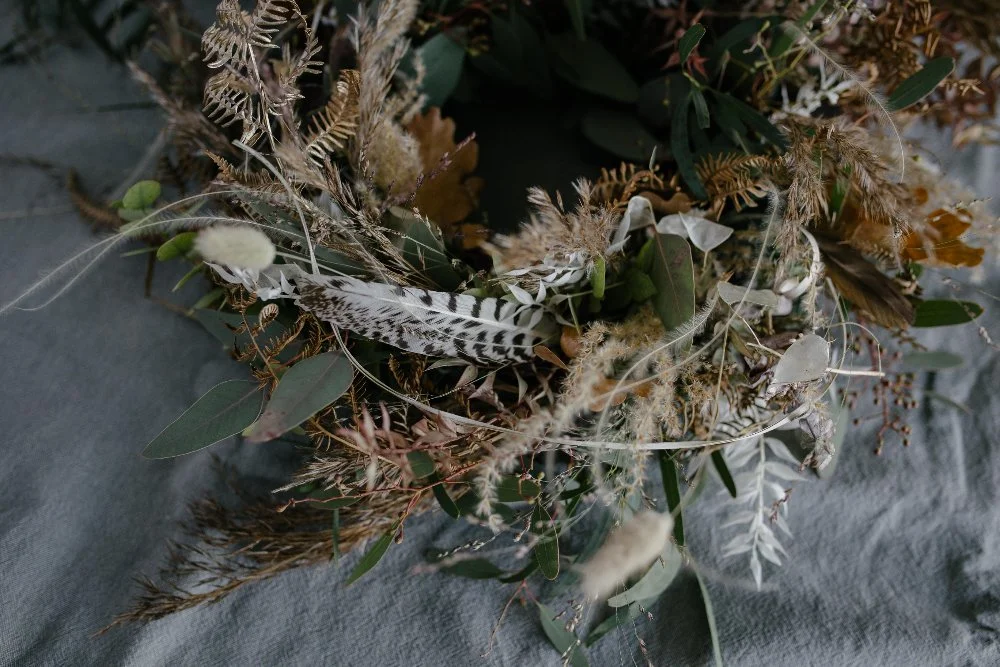 Ein Trockenblumenstrauß mit Federn und getrockneten Pflanzen auf einem grauen Stoffhintergrund