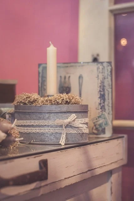 Ein runder Blechkasten mit Spitze und Schleife, eine Kerze, getrocknete Blumen.