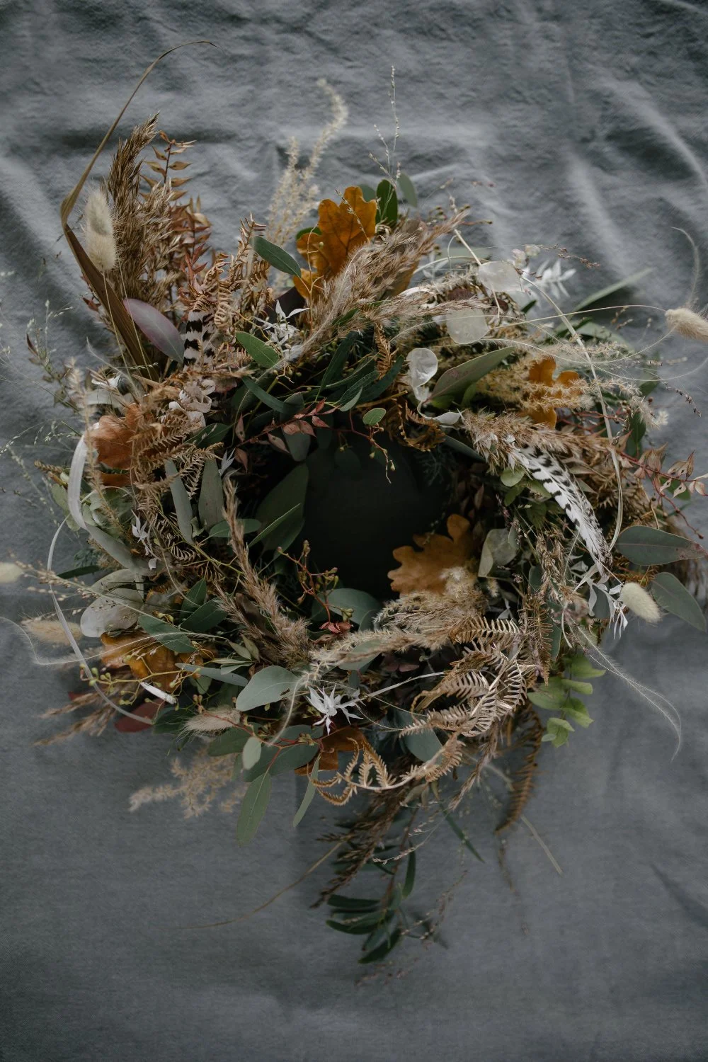 Ein Herbststrauss mit getrockneten Blättern, Federn und Gräsern auf einem grauen Stoffhintergrund.