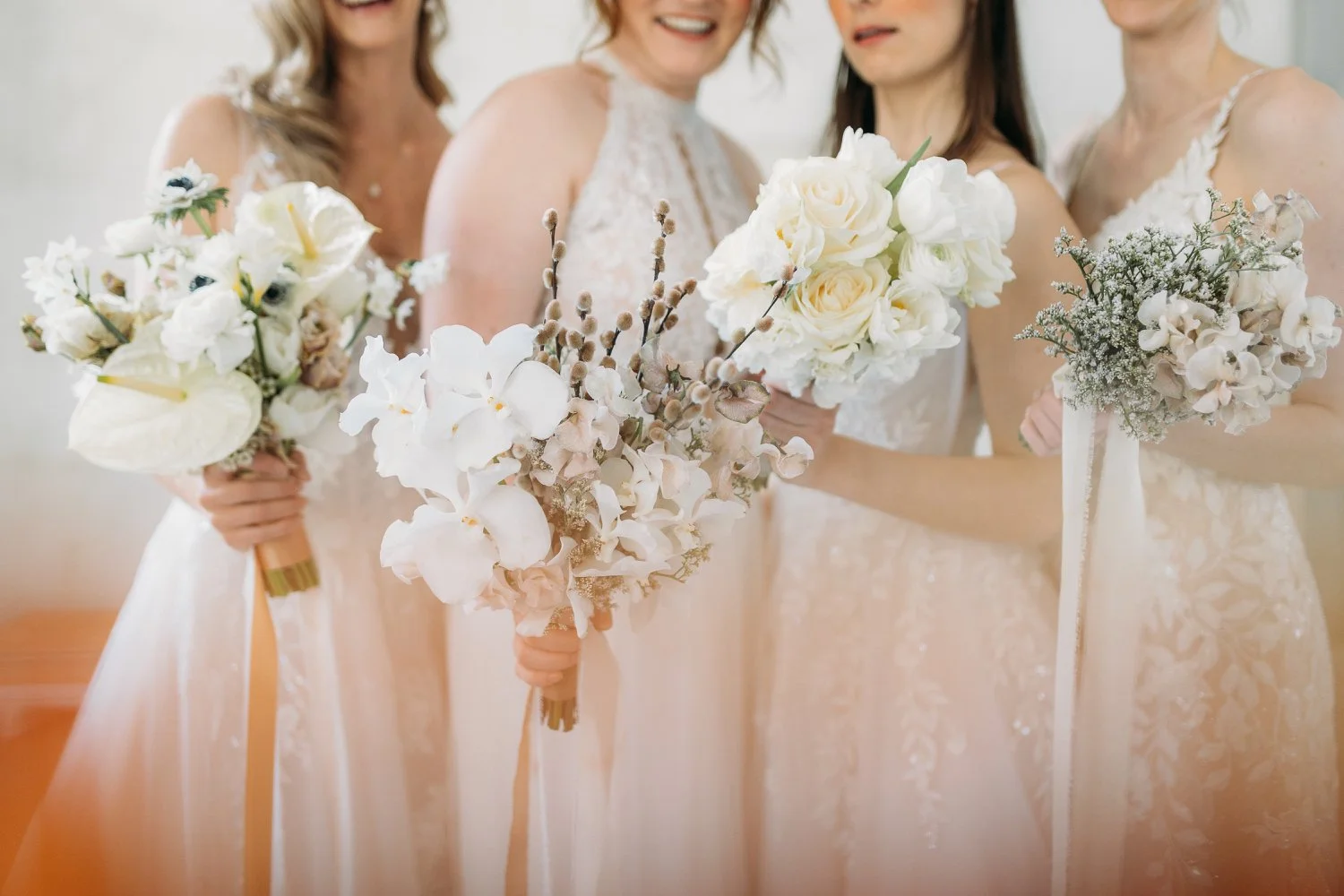 Vier Frauen in weissen Brautkleidern halten Blumengebinde bei einer Hochzeit.