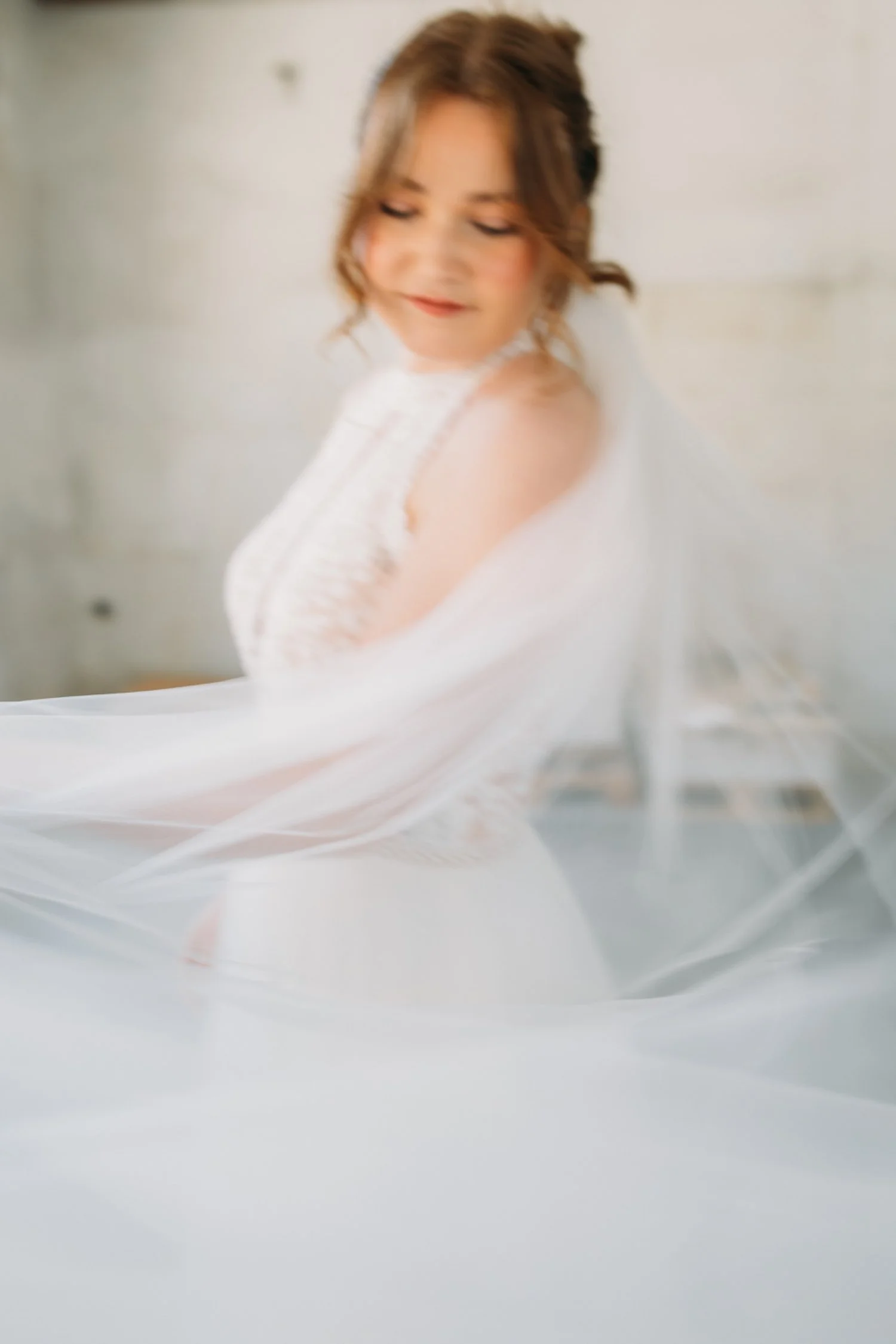 Eine lachende Braut in einem weissen Brautkleid mit Schleier vor einem grau-weissen Hintergrund.