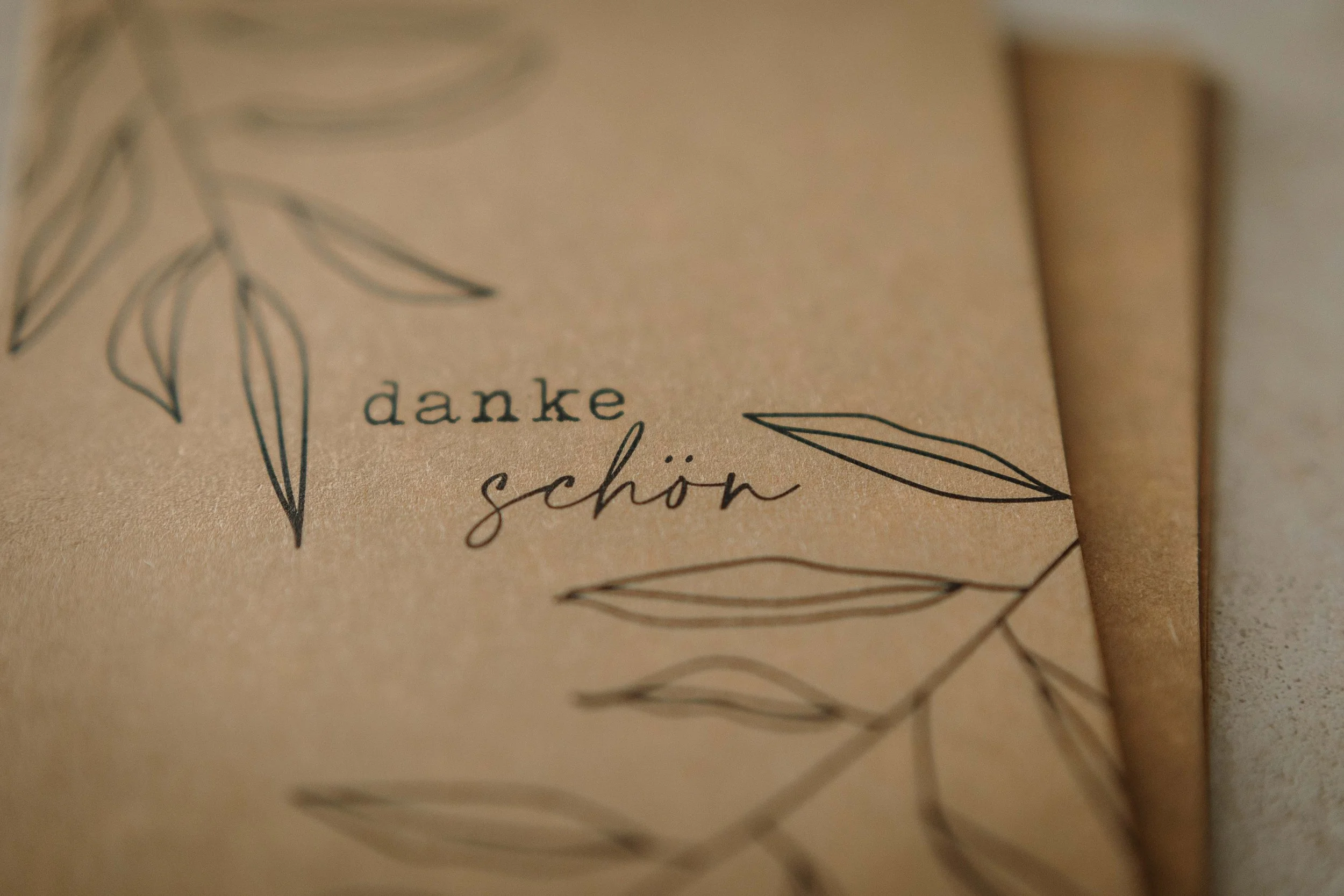 Nahaufnahme einer Postkarte aus braunem Papier mit der Aufschrift 'dankeschön' und handgezeichneten Blättern.