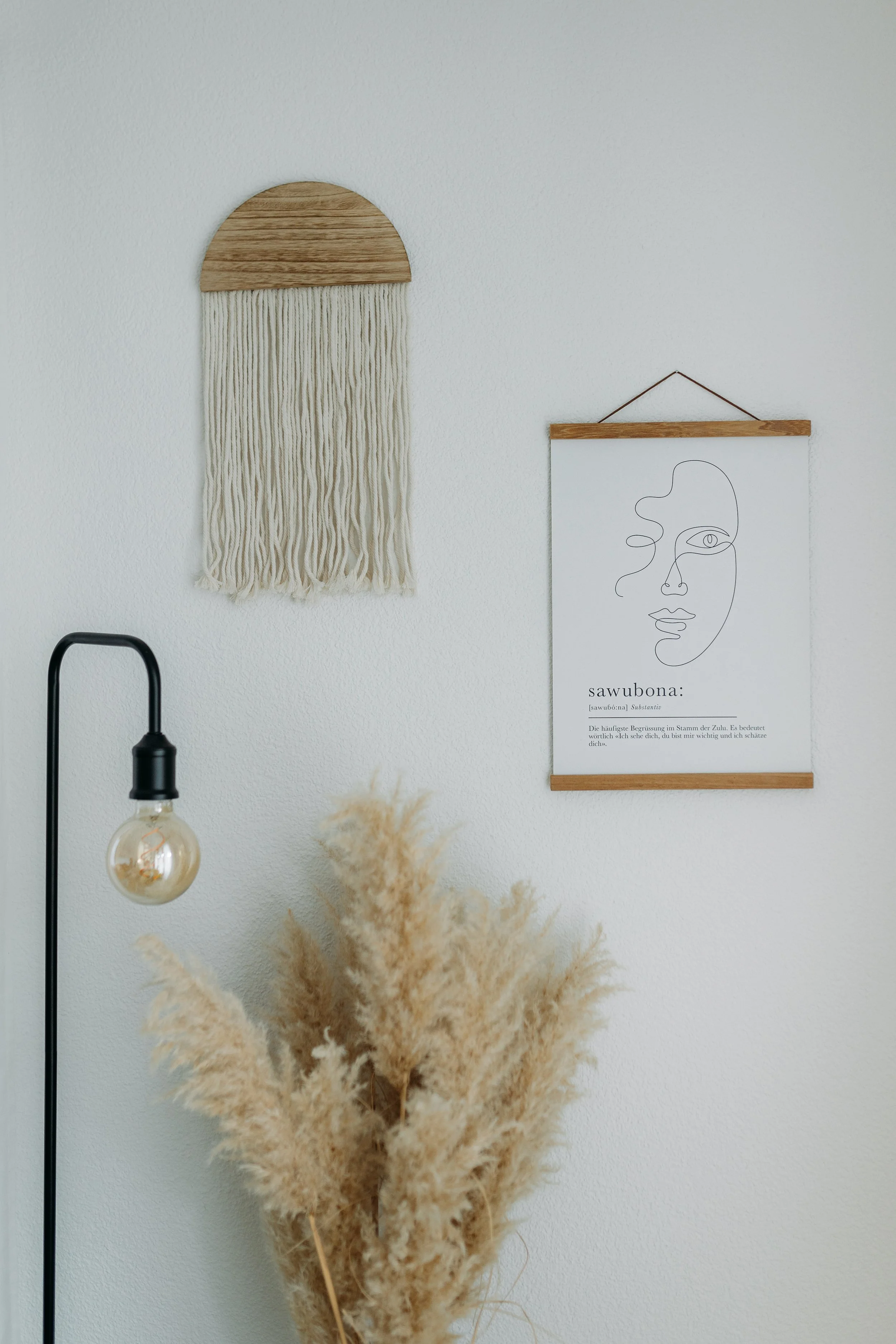 Moderner Wohnraum mit Wanddeko, Stehlampe mit Glühbirne, getrocknetem Pampasgras und einer Wandillustration.