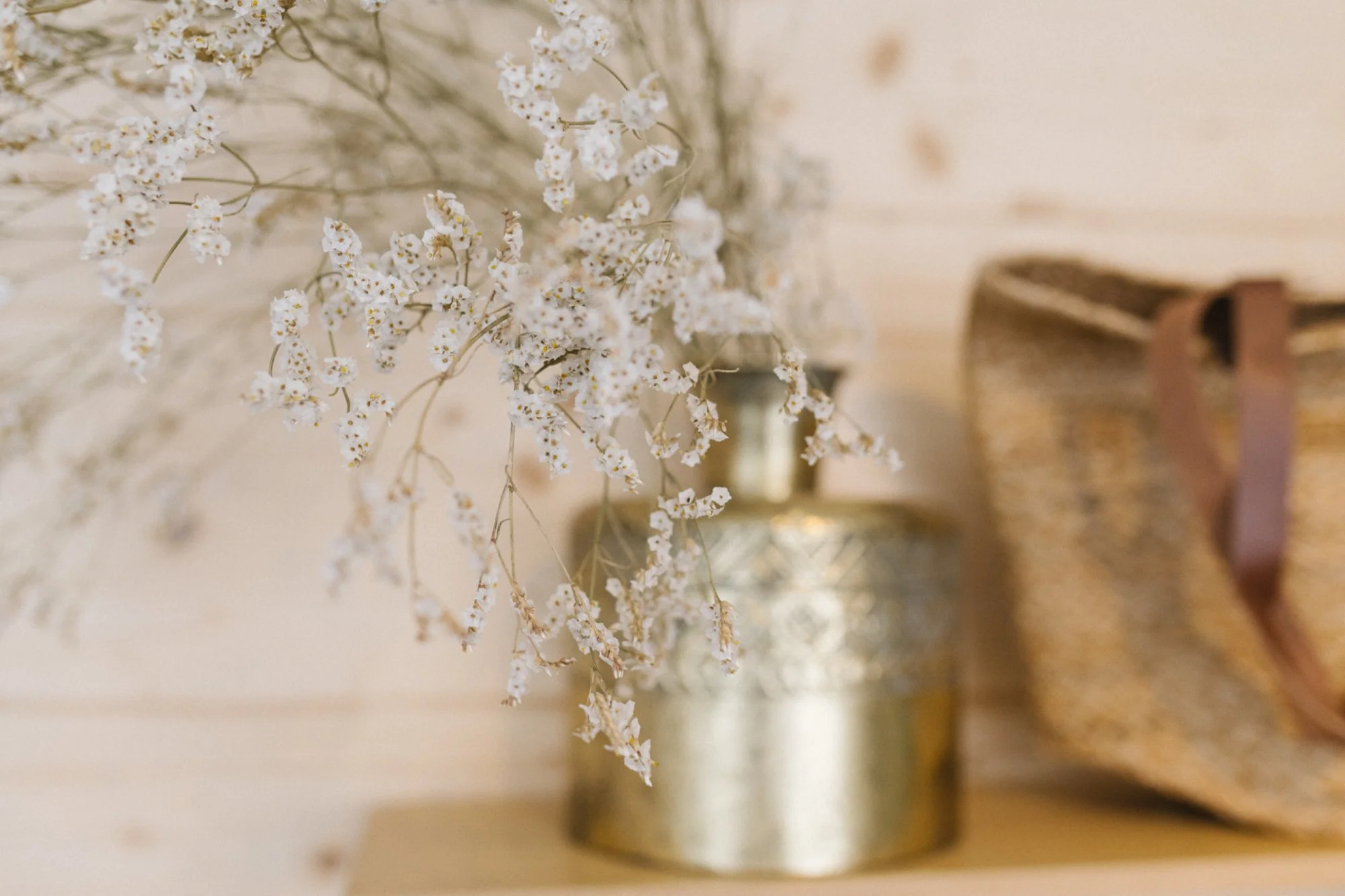 Blumen in einer silbernen Vase, daneben ein geflochtener Korb, auf einer Holzoberfläche vor einem hellen Holzhintergrund.