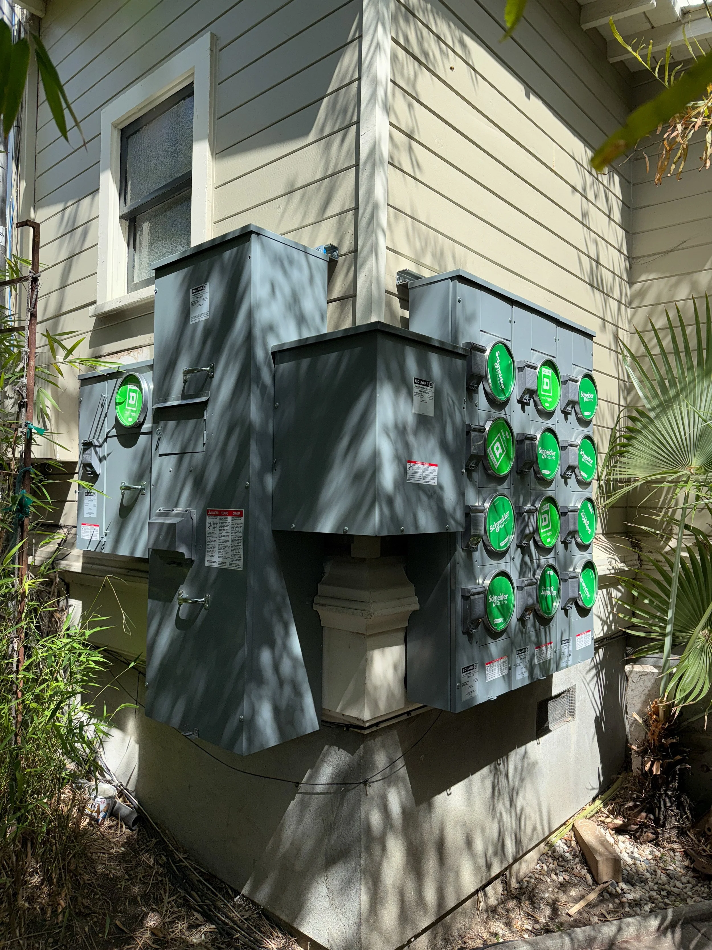 A 13 meter 200 amp main electrical service for a 13 unit apartment building, mounted in a tricky location where there is limited space, wraps around a corner in order to clear obstacles