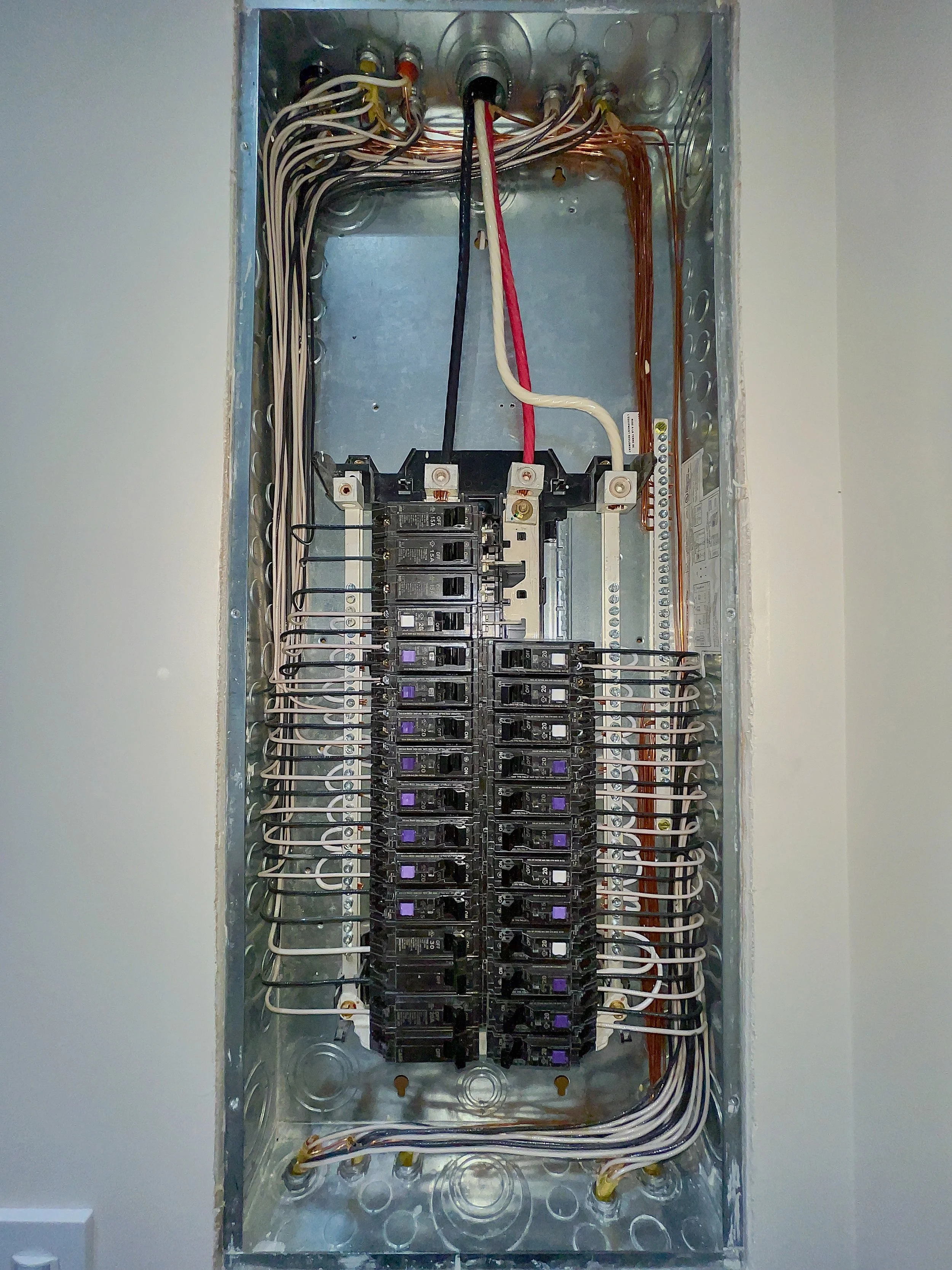 An electrical breaker panel with wiring and circuit breakers installed inside a metal box.