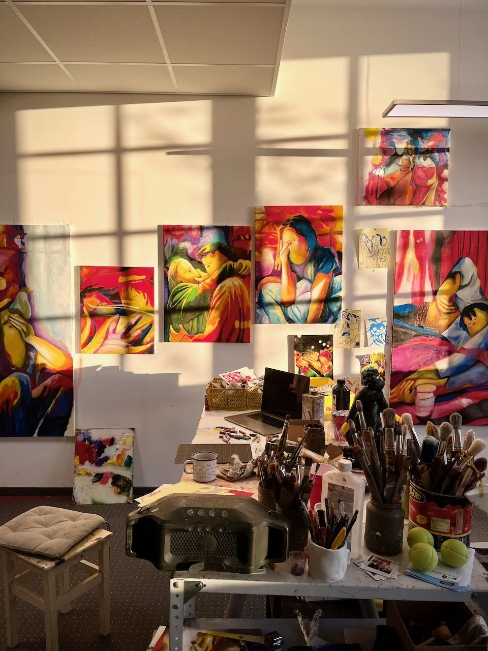 Am Arbeitsplatz der Münchner Malerin Nina Bachmann. Kunstwerke im Hintergrund, Pinsel und Computer im Vordergrund.