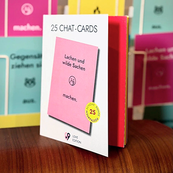 Taschenbuch mit 25 Chat-Karten auf einem Holztisch, darunter eine pinke Karte mit dem Text 'Lachen und wilde Sachen machen'.