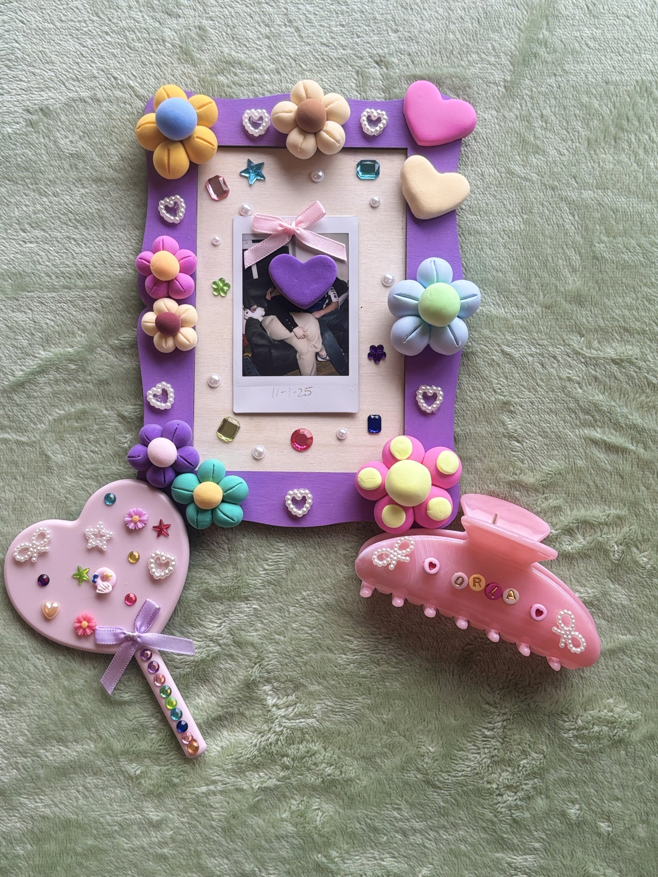 Decorative photo frame surrounded by colorful jewelry and craft items on a textured green surface.