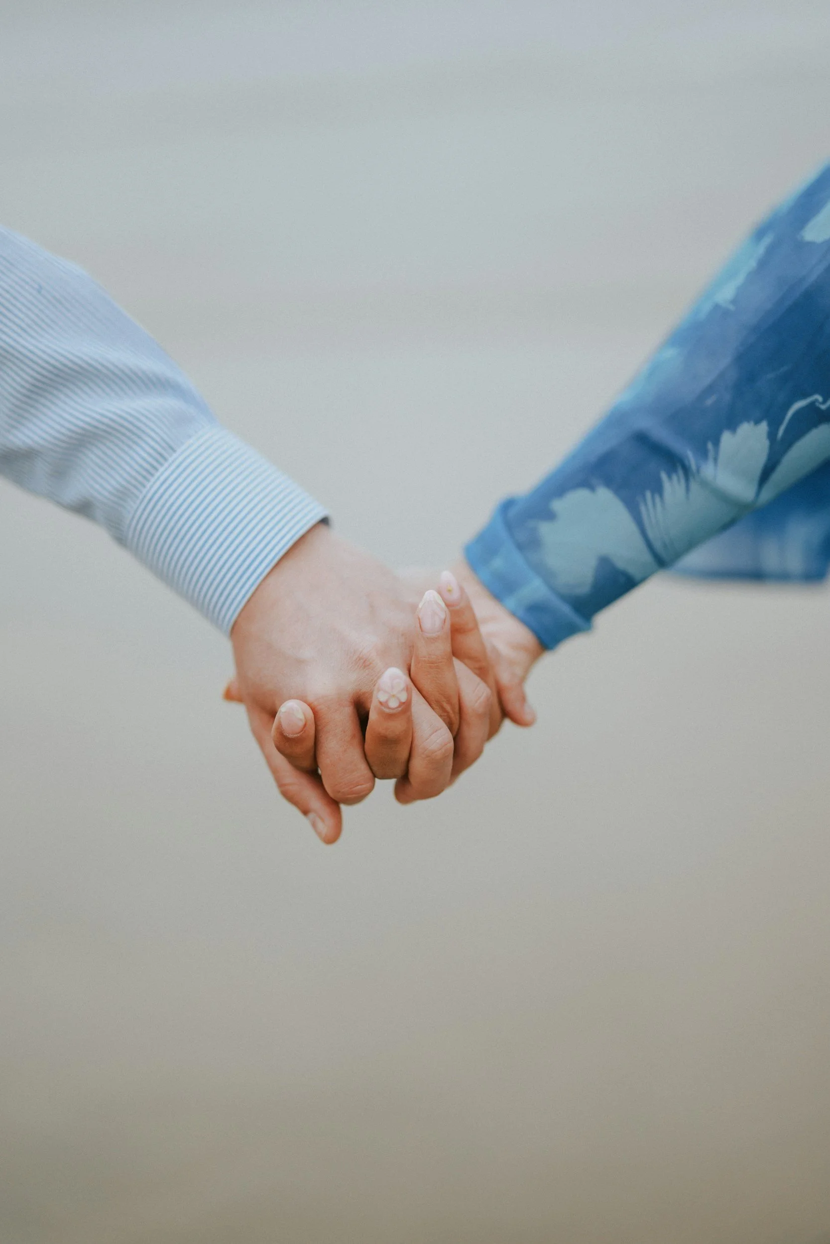 Two people holding hands, one in a striped shirt and the other in a blue patterned shirt.