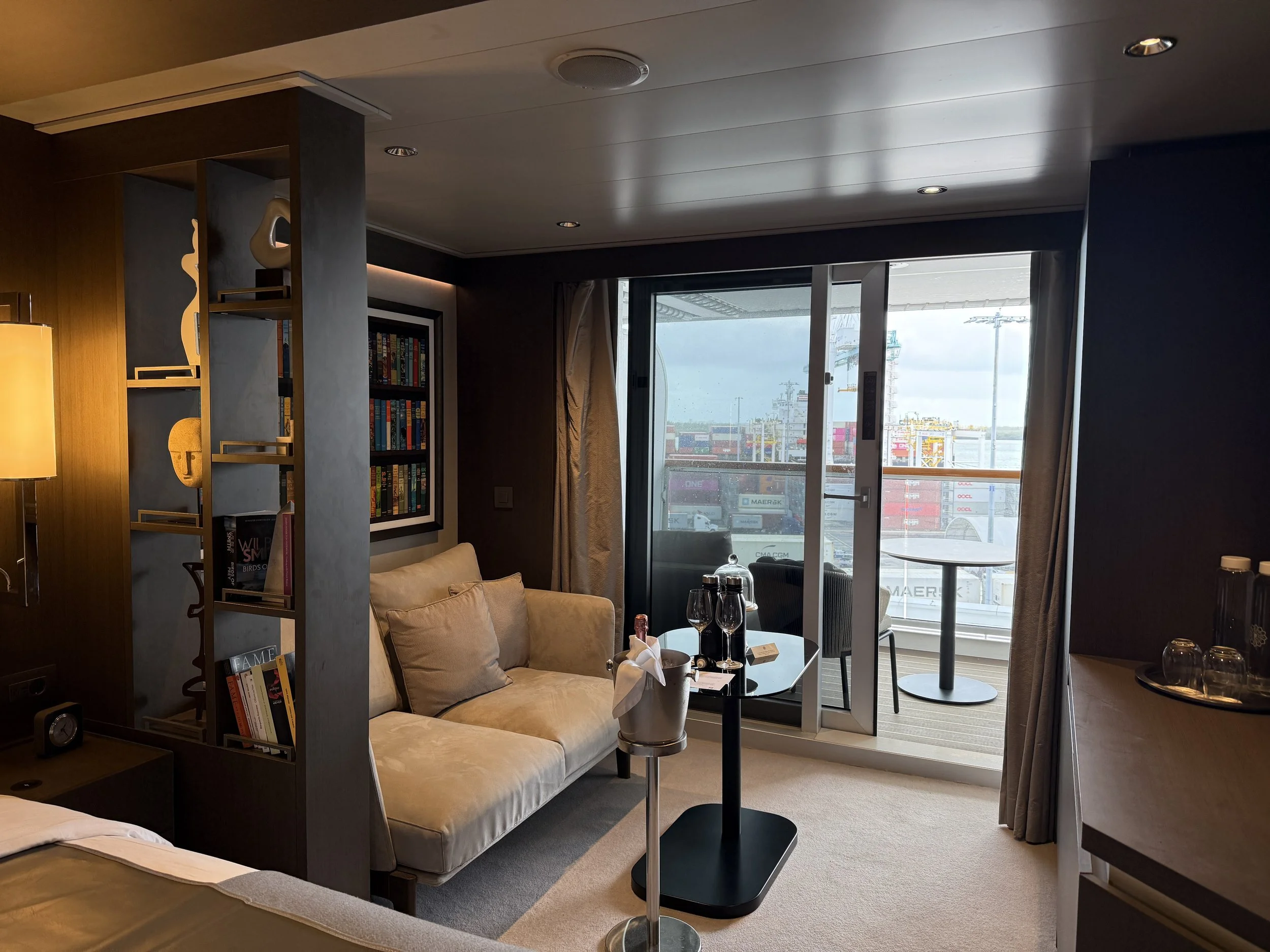 Explora Journey's ocean terrace suite with a curated bookshelf, plush seating, and a private terrace