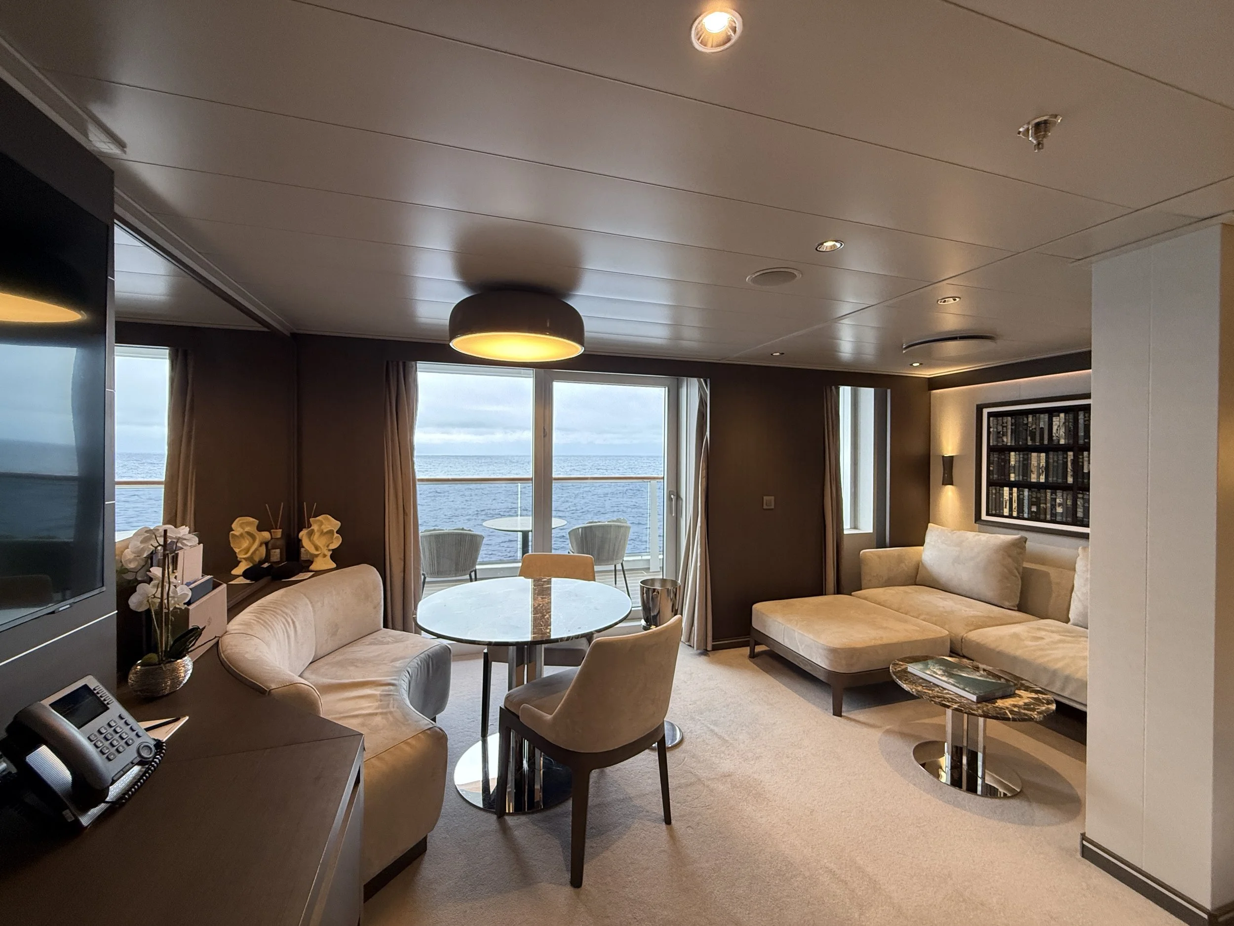 Interior of an all-suite Explora Journeys deluxe penthouse suite with lounge seating and floor-to-ceiling windows over the sea