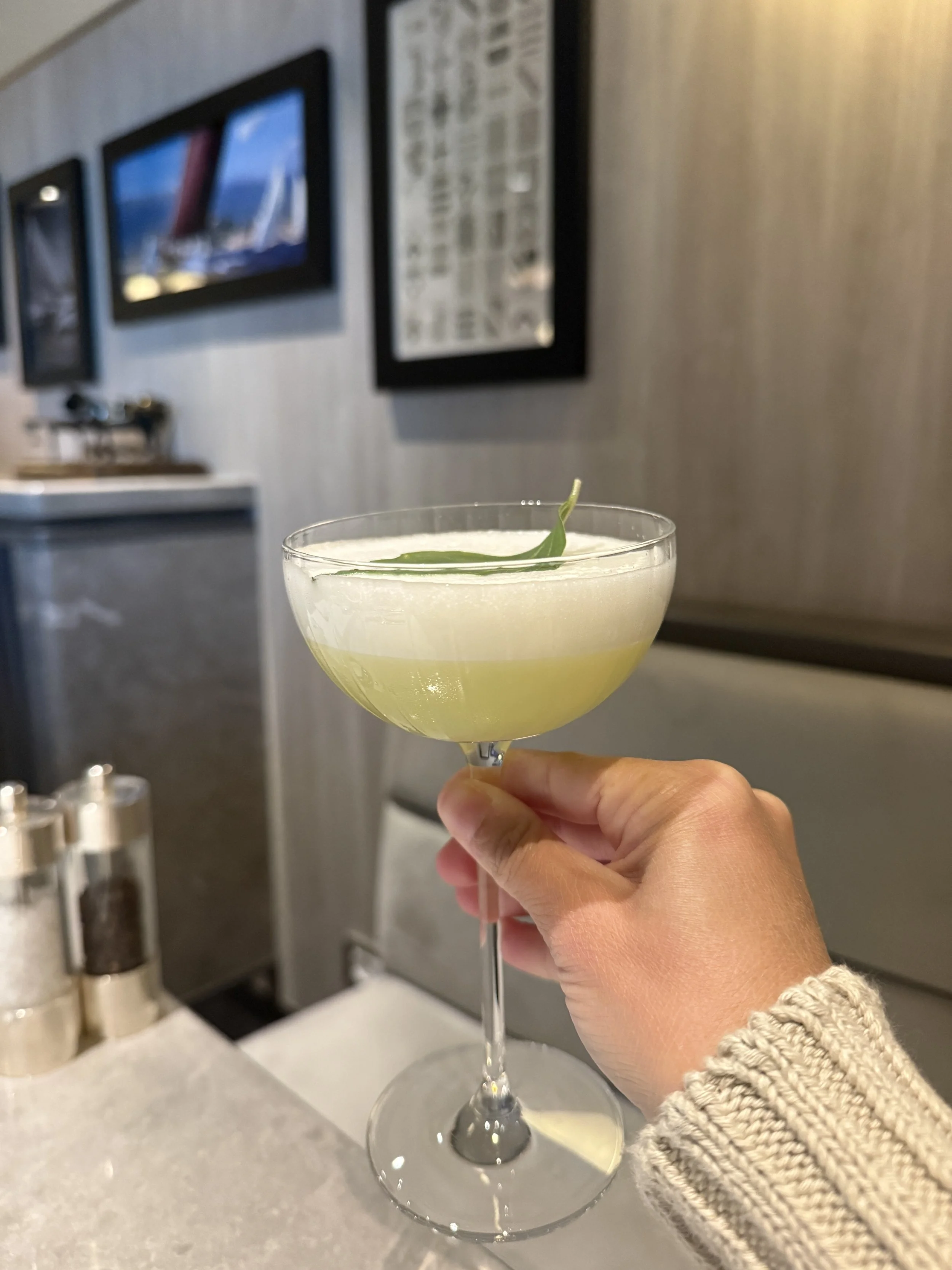 Hand holding a frothy craft cocktail garnished with a fresh herb leaf aboard Explora Journeys