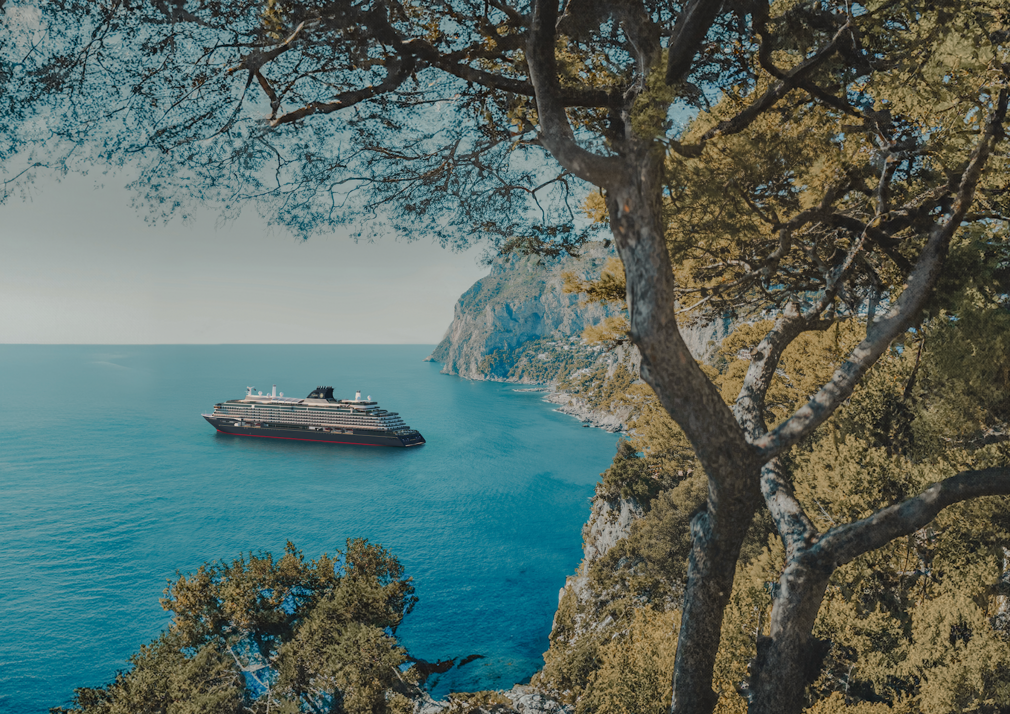Explora Journeys ship at anchor in a calm turquoise cove, framed by pine trees and rocky Mediterranean cliffs