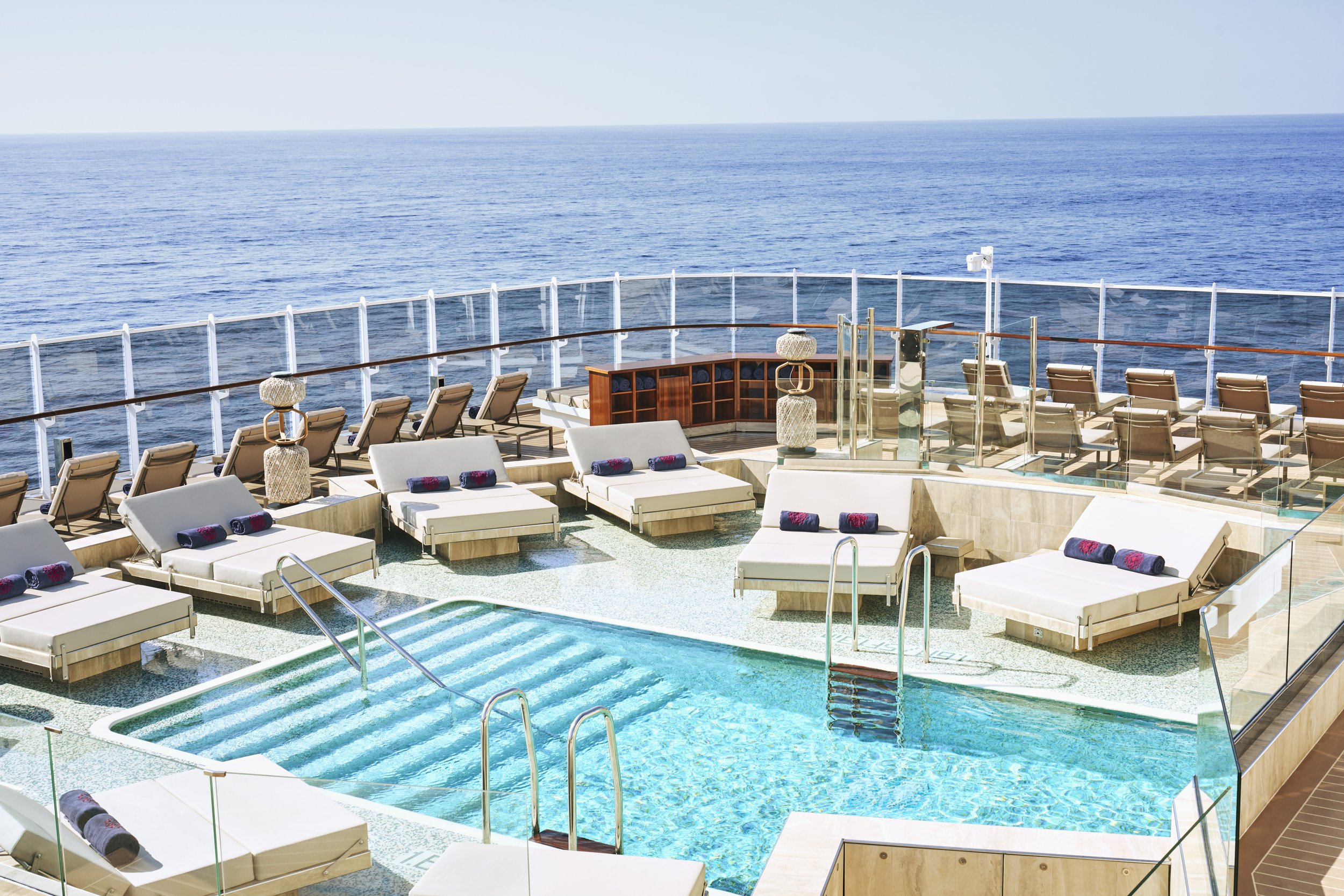 A pool deck aboard EXPLORA I with an open-air pool, plush double loungers, and uninterrupted views of the open ocean