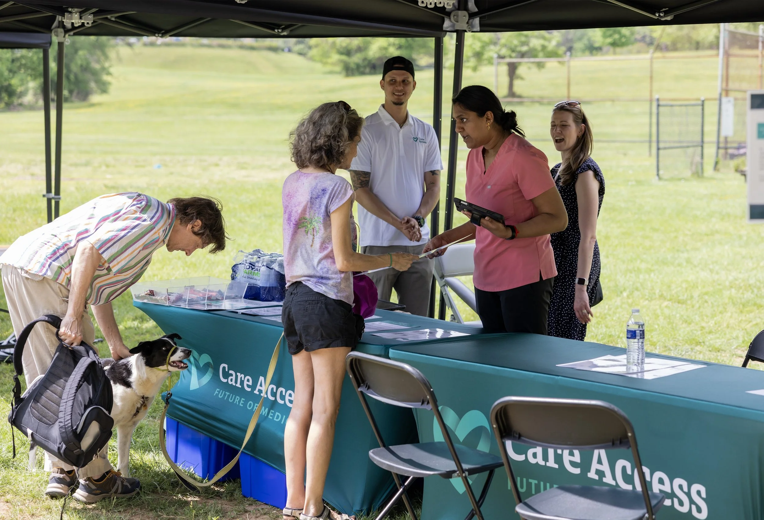 People at a Care Access health screening booth outdoors, learning about the Future of Medicine Community Health Screening program.